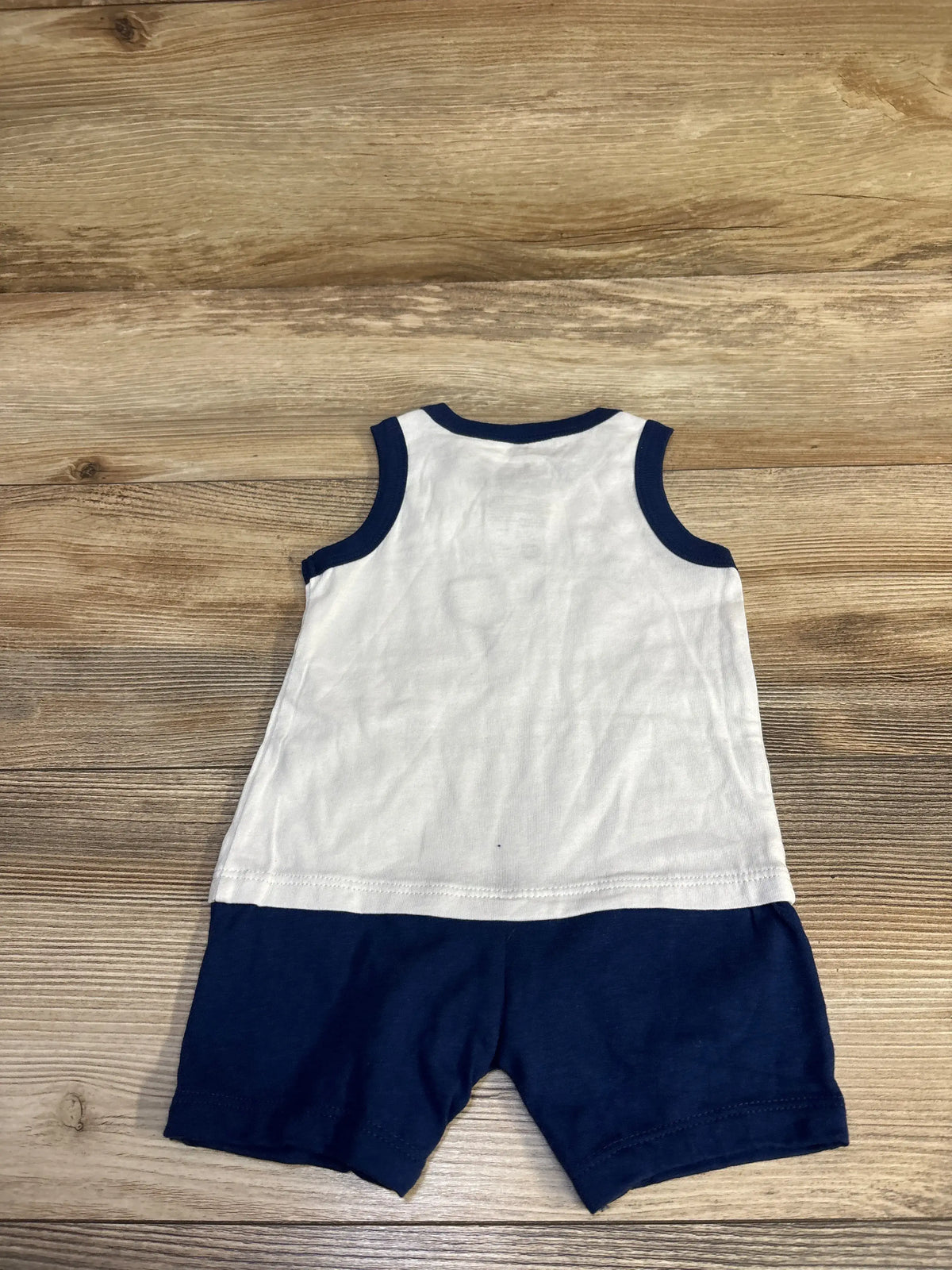 Back view of First Impressions Good Sport shortie romper, white sleeveless top with navy trim and attached navy shorts on wood