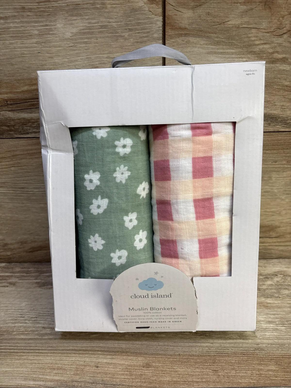 Front view of Cloud Island 2pk muslin swaddle blankets showing green floral and pink gingham patterns in a box on wood