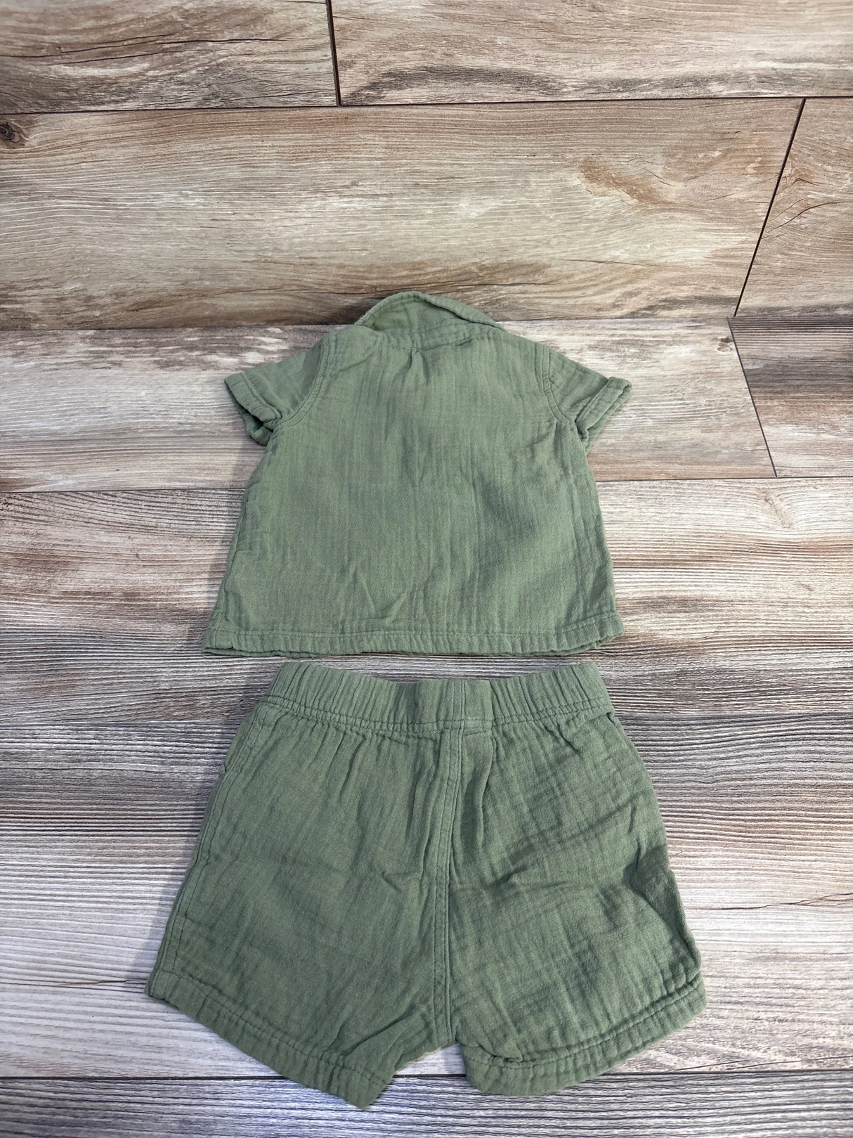 Flat lay of green gauze Henley shirt and elastic-waist shorts set 6-12M, short sleeves and textured fabric on wood background