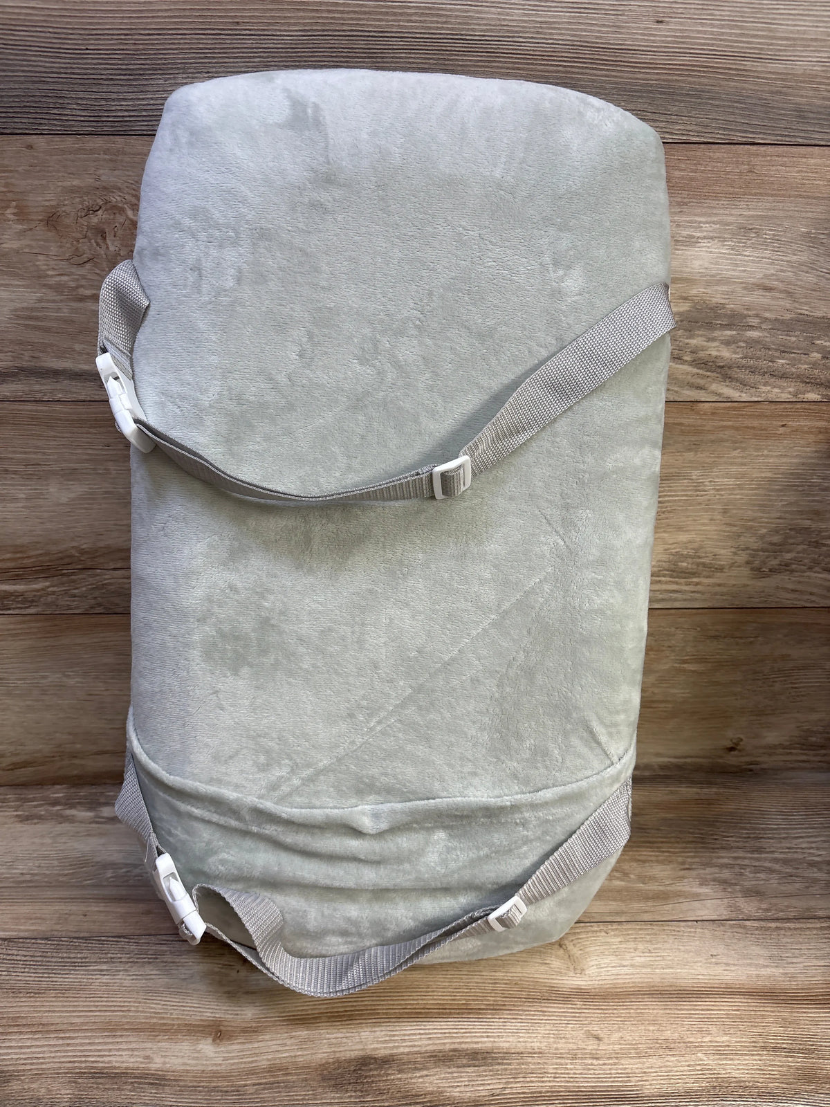 Top view of Babocush newborn comfort cushion showcasing light gray plush cover and adjustable gray straps with white buckles on wood plank background