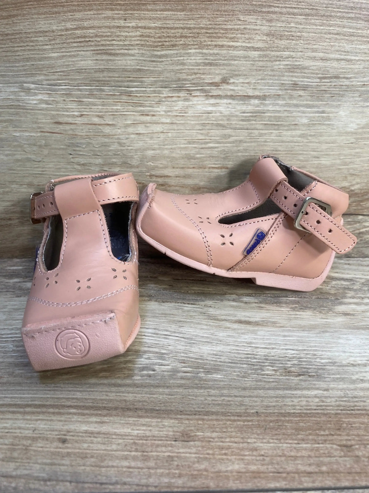 Pink leather toddler shoes with buckle straps and cutout floral details on wood background