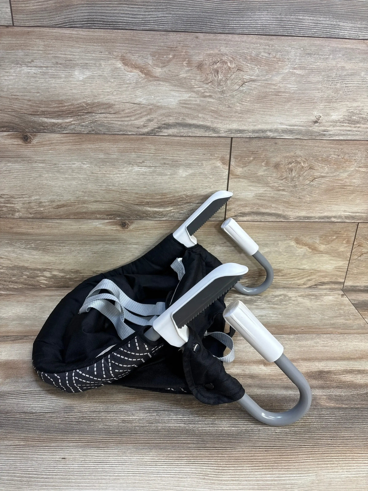 Three-quarter view of MTWML Hook On High Chair in black stripe showing folded grey clamps and safety straps on wood floor