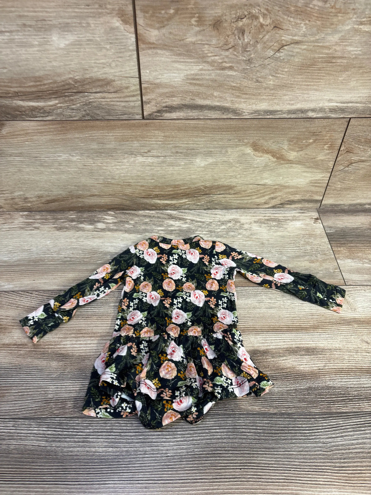 Front view of Gigi & Max bamboo floral tutu bodysuit in black showcasing long sleeves and tutu skirt with a wood-look background