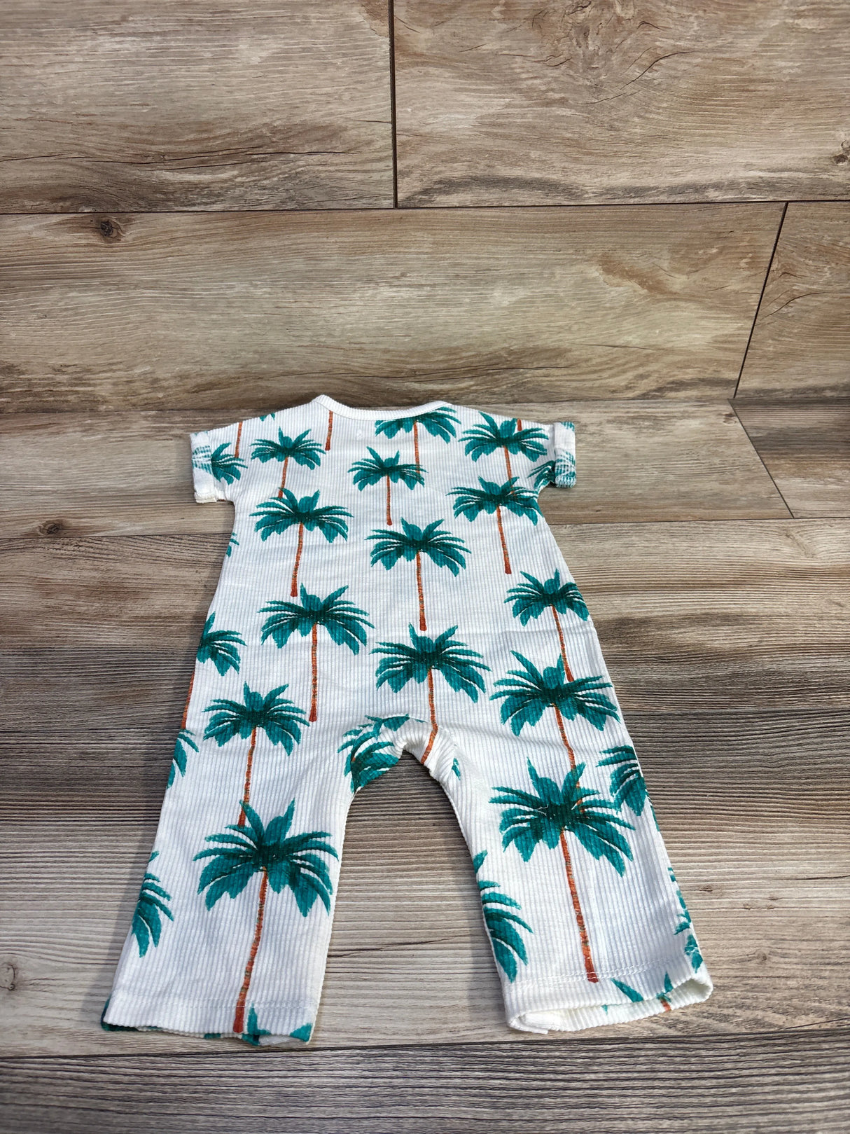 Flat lay of white Grayson Mini palm tree ribbed jumpsuit showcasing green palm print and short sleeves on wood background
