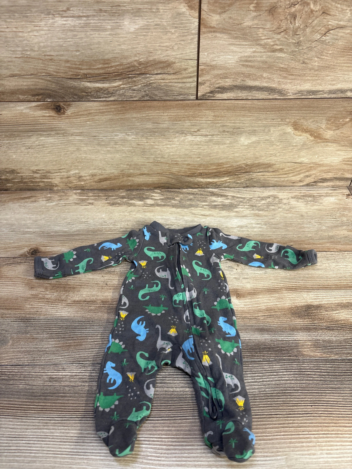 Front view of preemie grey footed sleeper showcasing colorful dinosaur print and front zipper on wooden background
