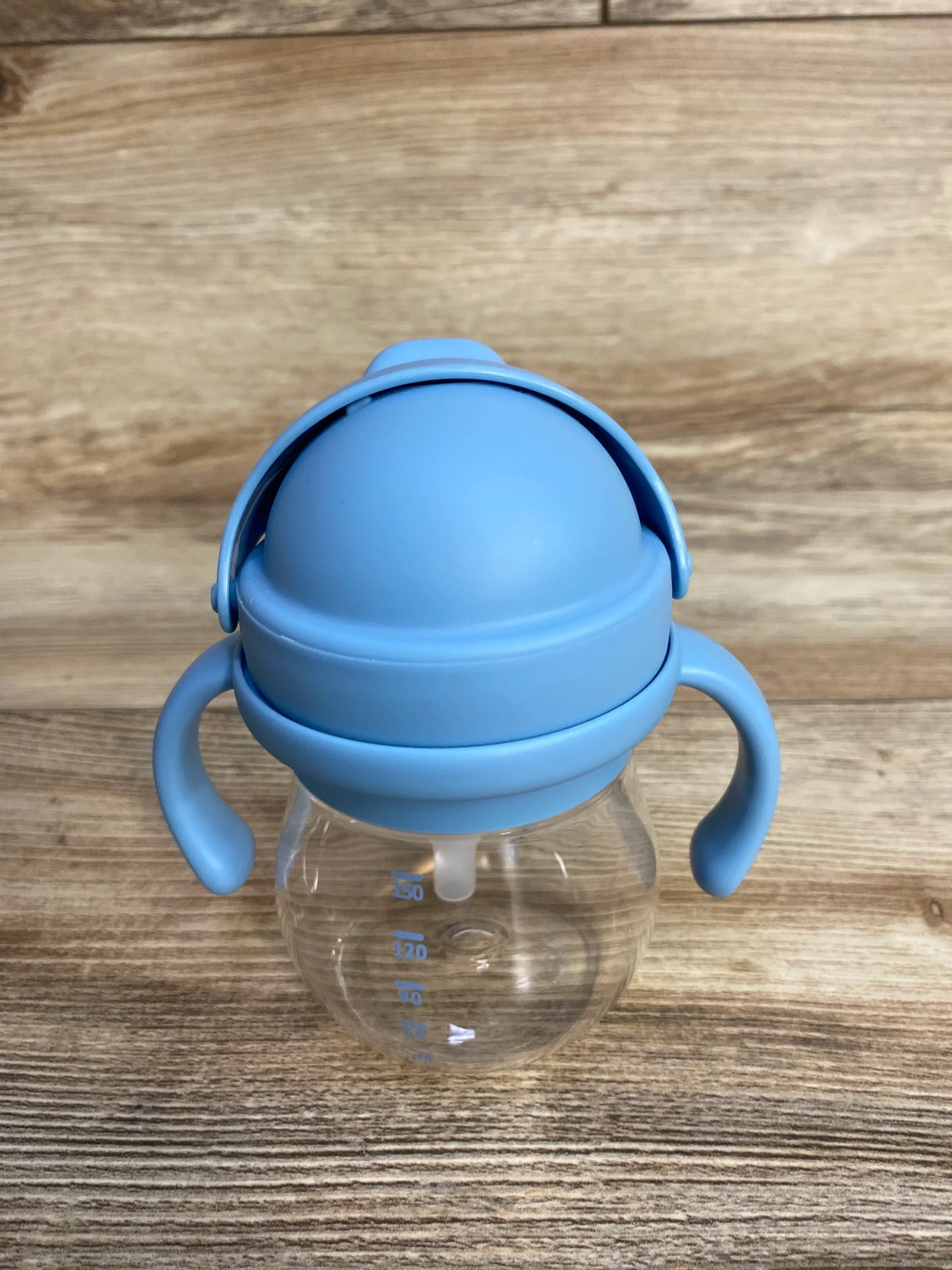 Blue handled baby sippy cup with measurement markings on wood background