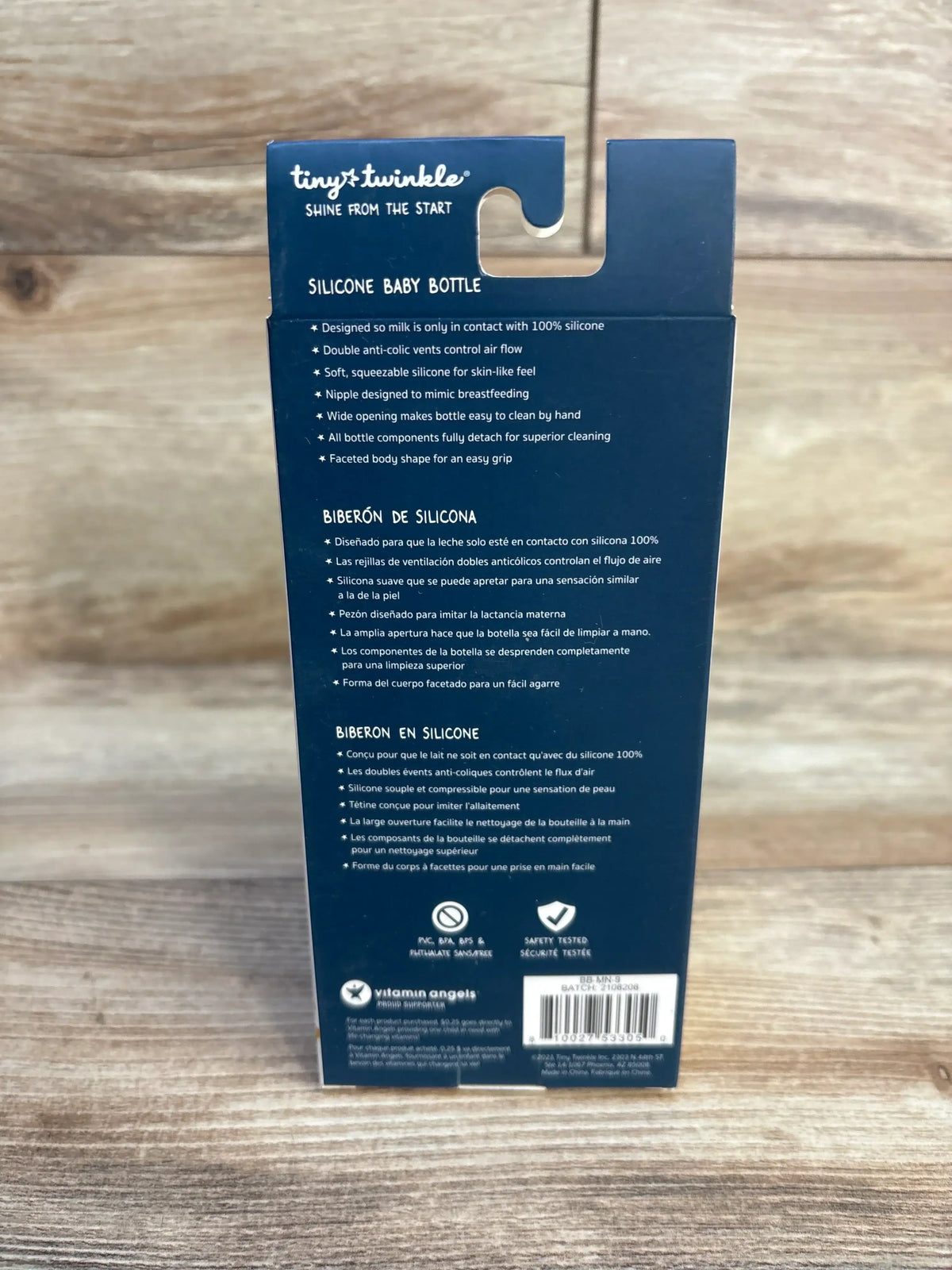 Rear view of Tiny Twinkle silicone baby bottle box showing product features and safety icons on wood background