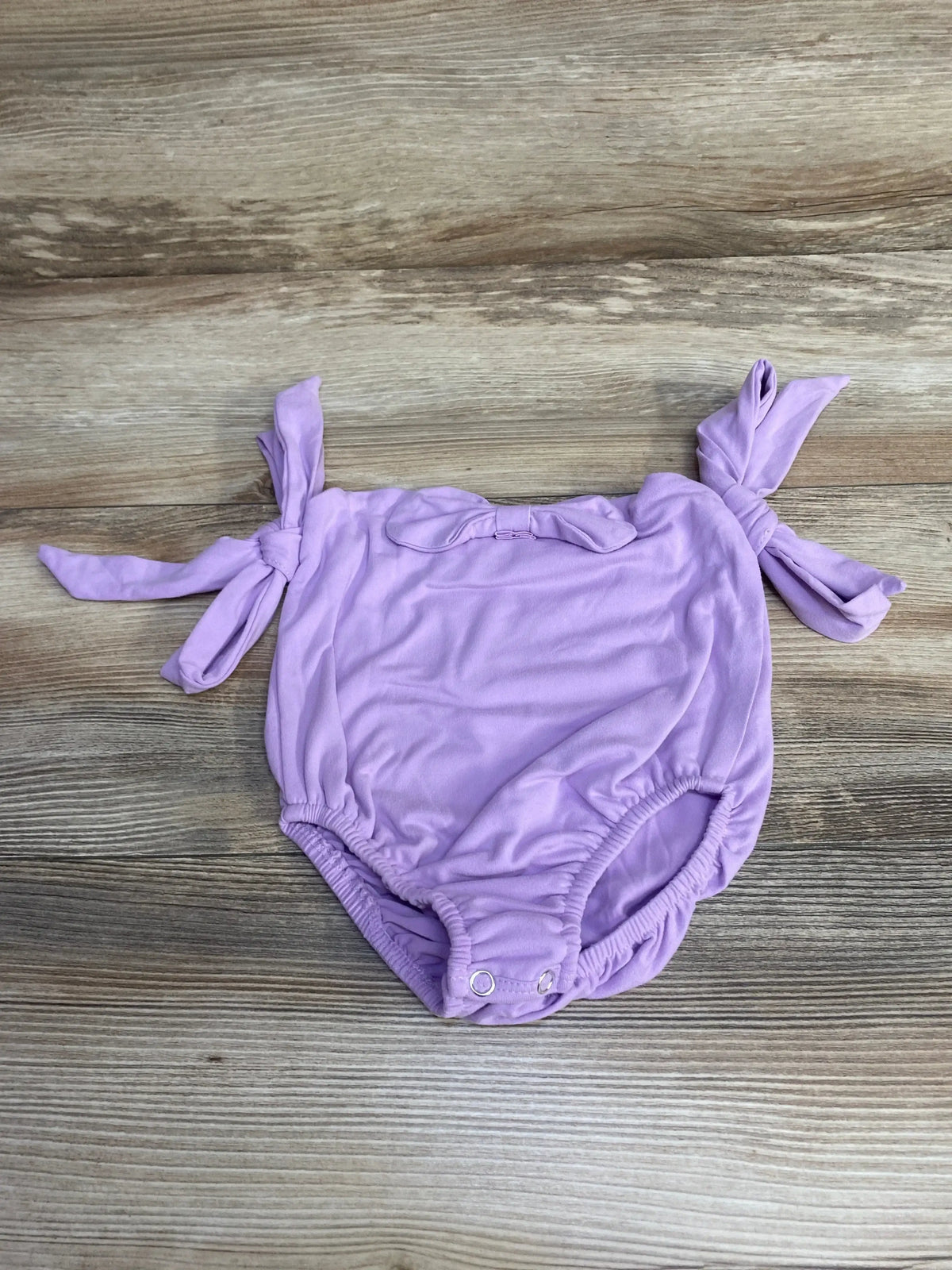 Flat lay of purple Baileys Blossoms sleeveless leotard size 2T, tied shoulder straps, front bow, snap crotch on light wood