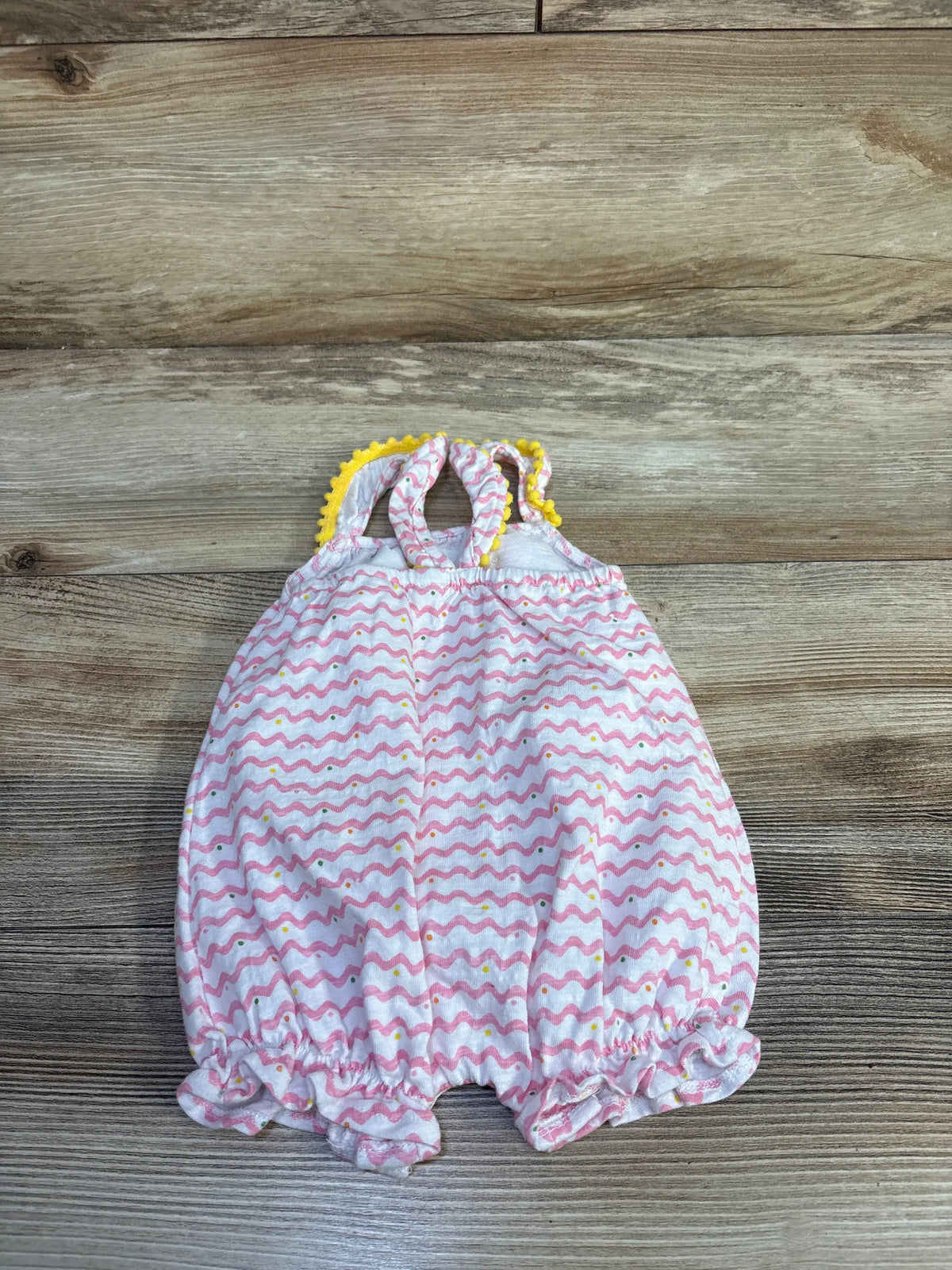 Top view of Mudpie chevron pom-pom fruit shortie romper in white, size 0-3 months, with yellow pom-pom trim on wood
