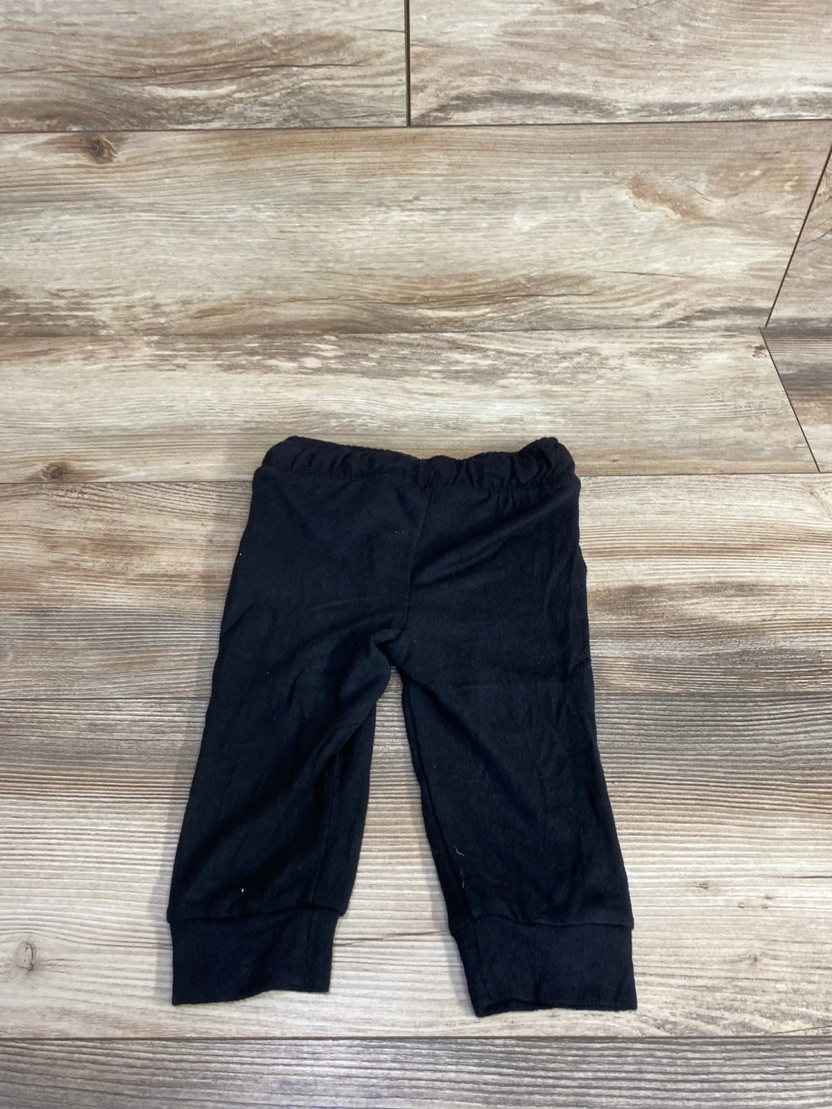 Black baby leggings with elastic waistband, laid flat on wood floor