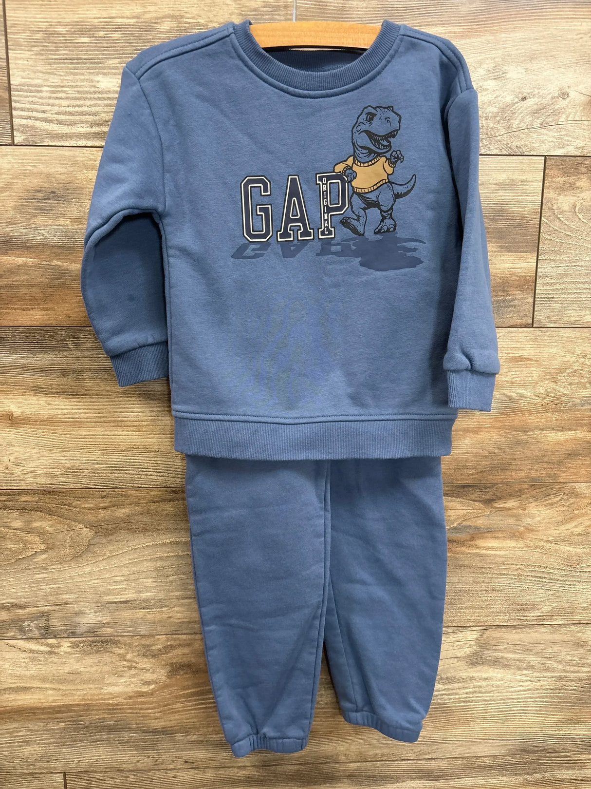 Blue toddler sweatshirt and pants set with dinosaur graphic and GAP logo on wood background