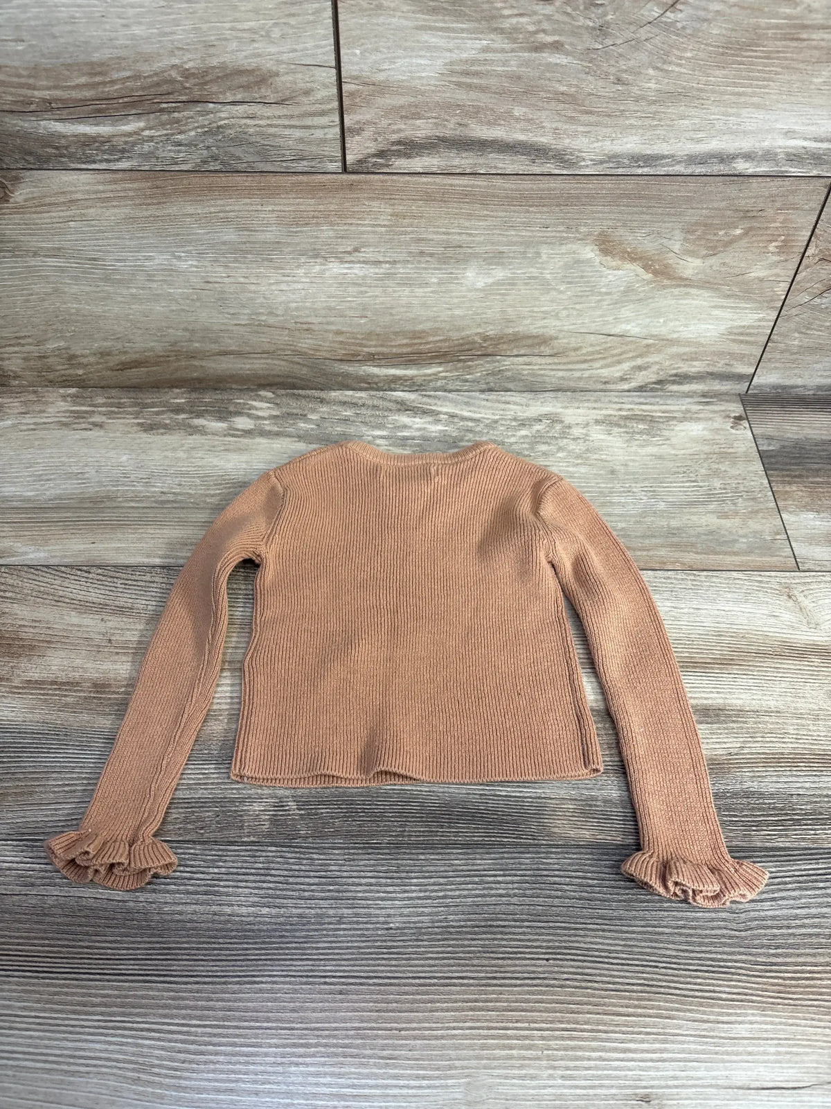 Back view of Tommy Bahama Ribbed Long Sleeve Shirt in tan showcasing ruffle cuffs and ribbed knit on wood plank floor