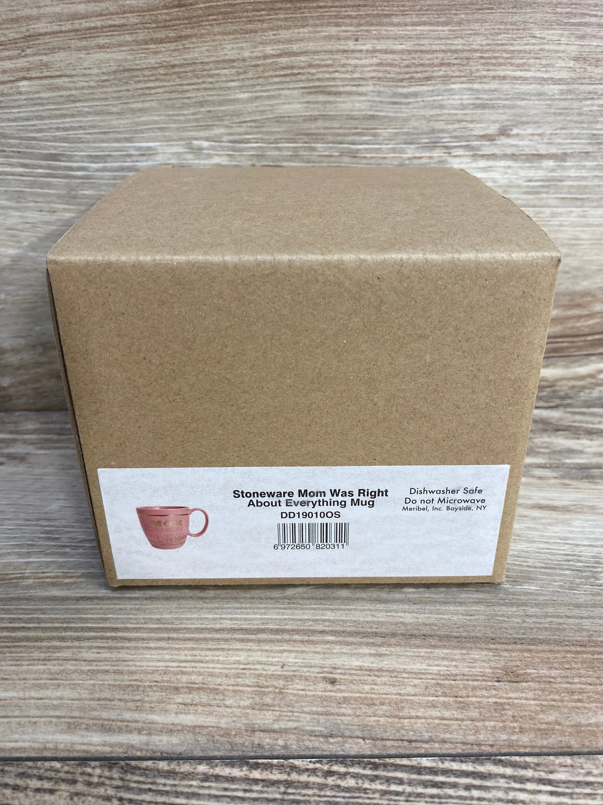 Front view of Stoneware Mom Was Right About Everything pink mug in unopened kraft brown shipping box with product label on wood plank floor