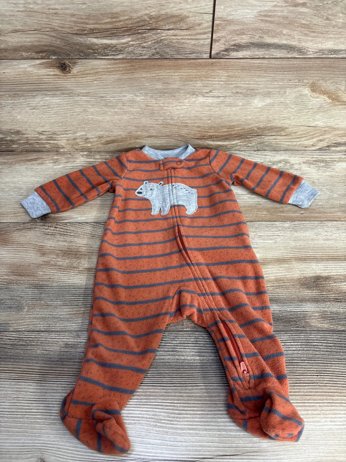 Orange and gray striped baby onesie with bear applique and footed legs on wooden floor