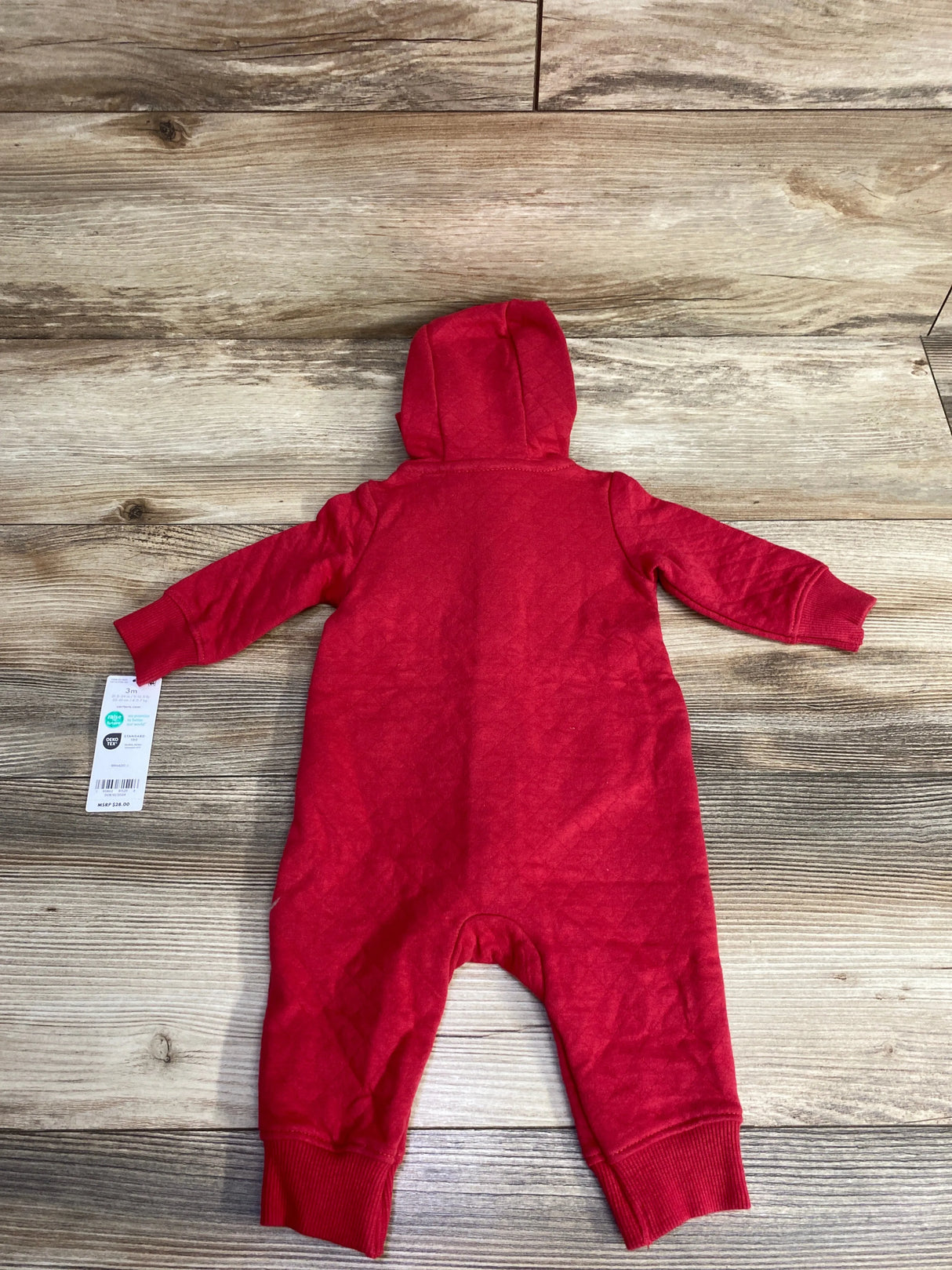 Red hooded baby romper laid flat on wood floor, long sleeves, ribbed cuffs, with size tag attached