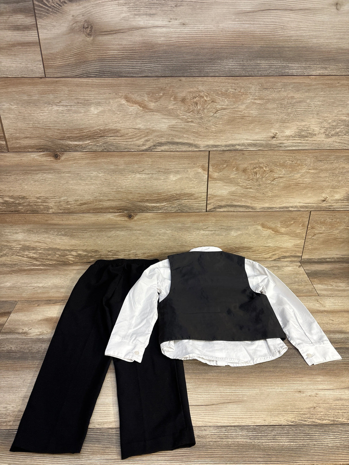 Children's formal outfit with black pants, white long-sleeve shirt, and black vest on wooden floor