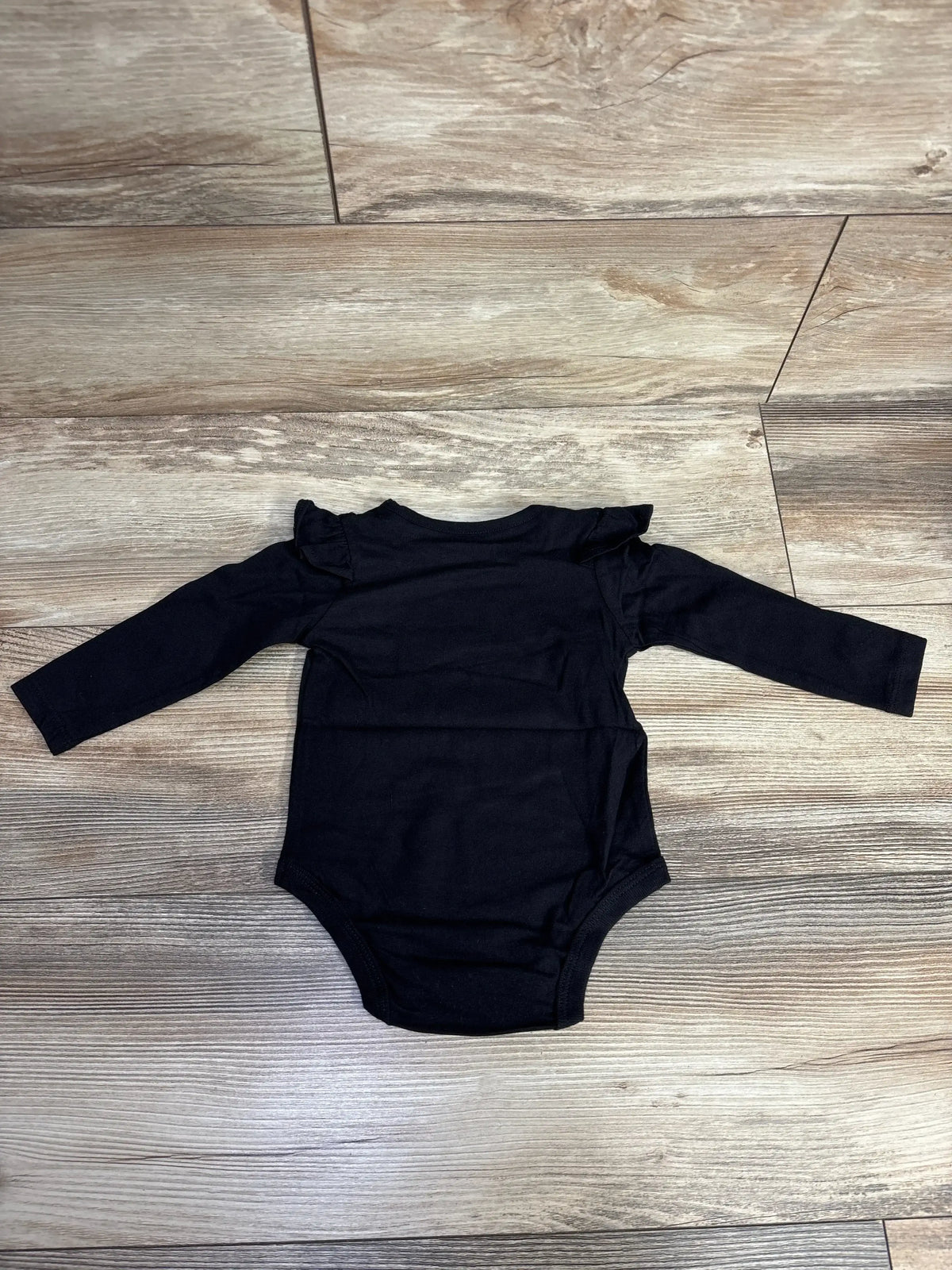 Black long-sleeve baby bodysuit with ruffle shoulder details on wood floor
