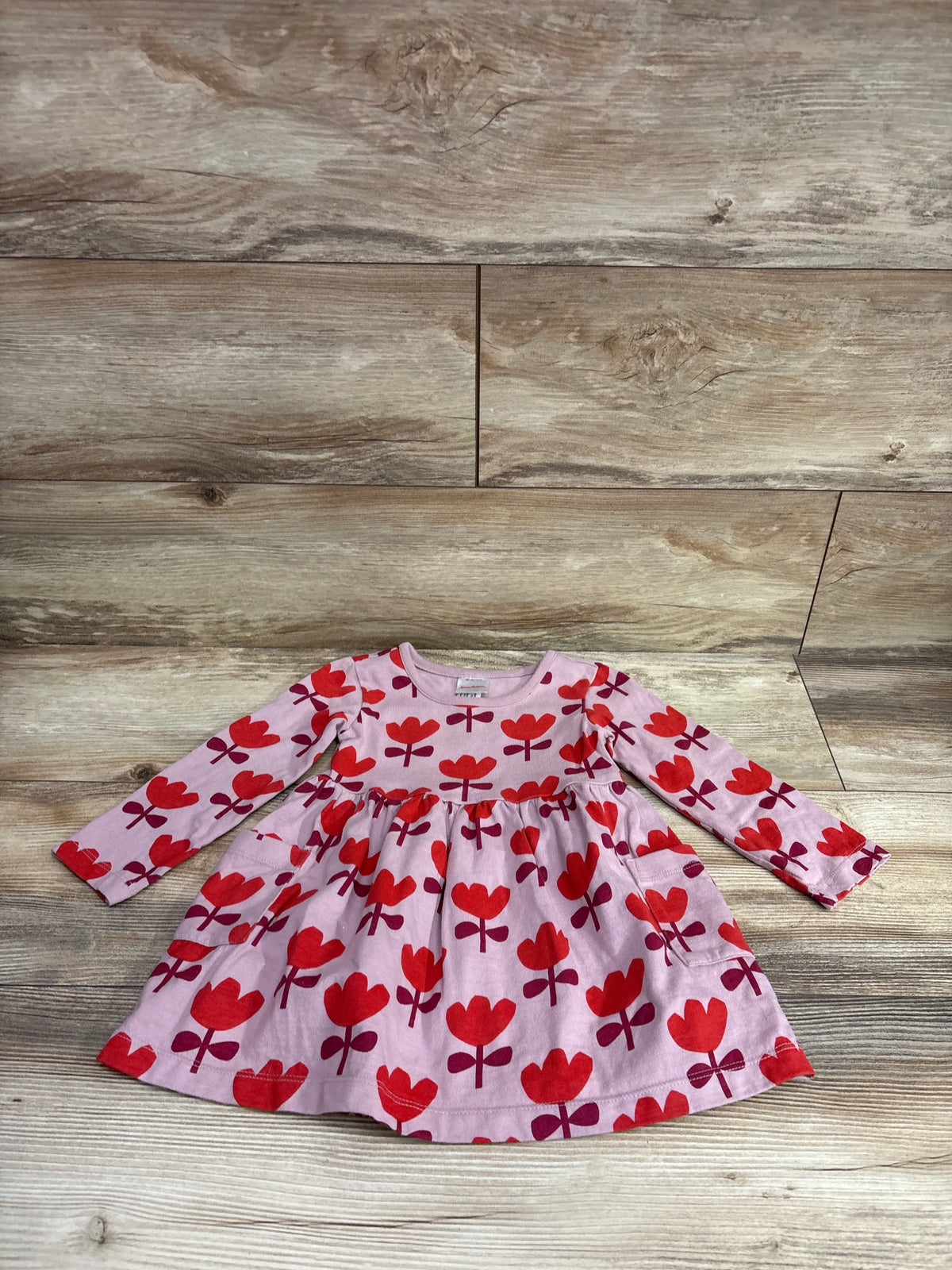 Front view of Hanna Andersson long sleeve tulip playground dress in dusty rose, showcasing red tulip print and pockets on a wood background