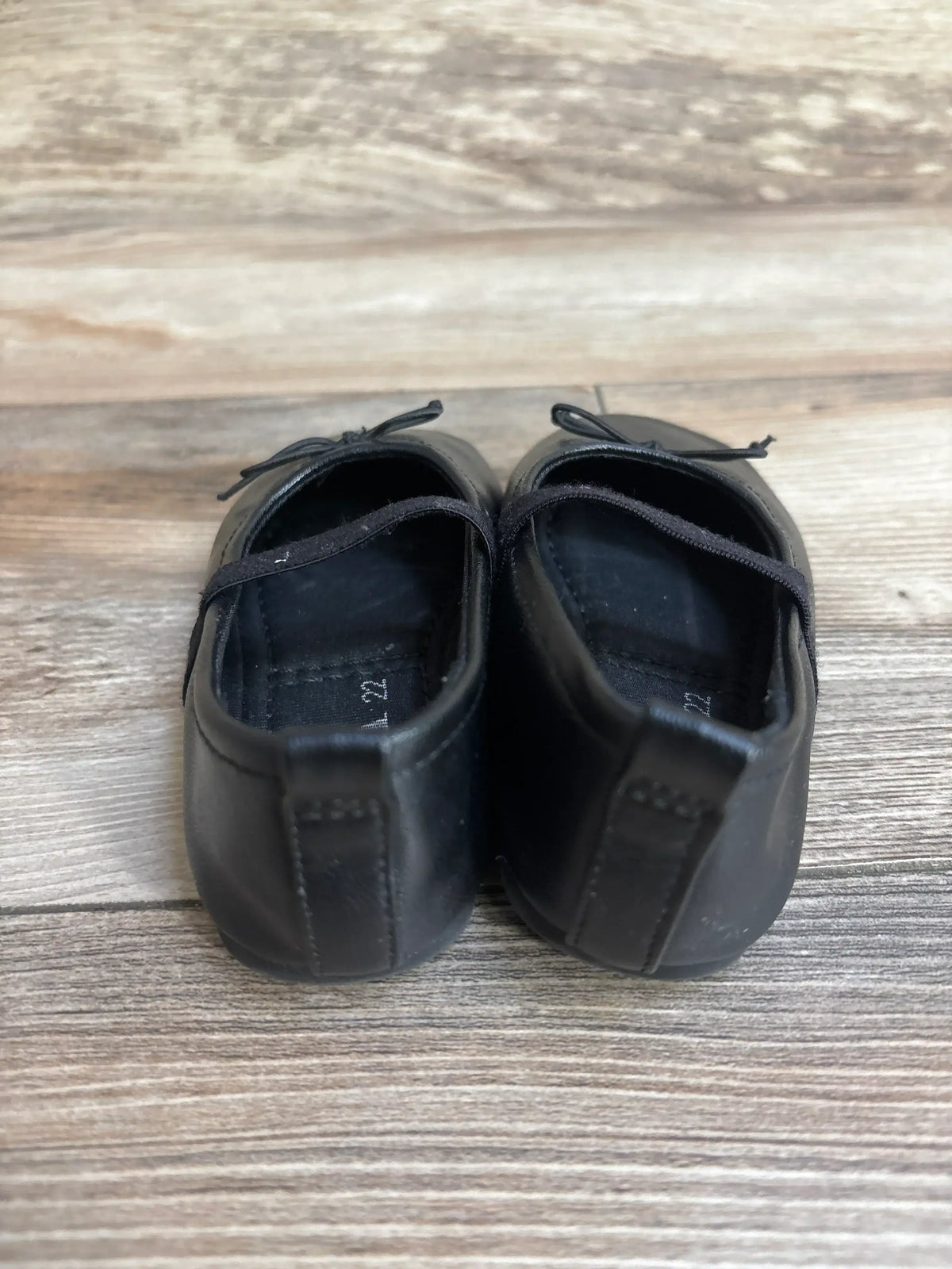 Rear view of Zara Mary Jane flats size 6C showing black leather, elastic strap and small bow on wooden floor