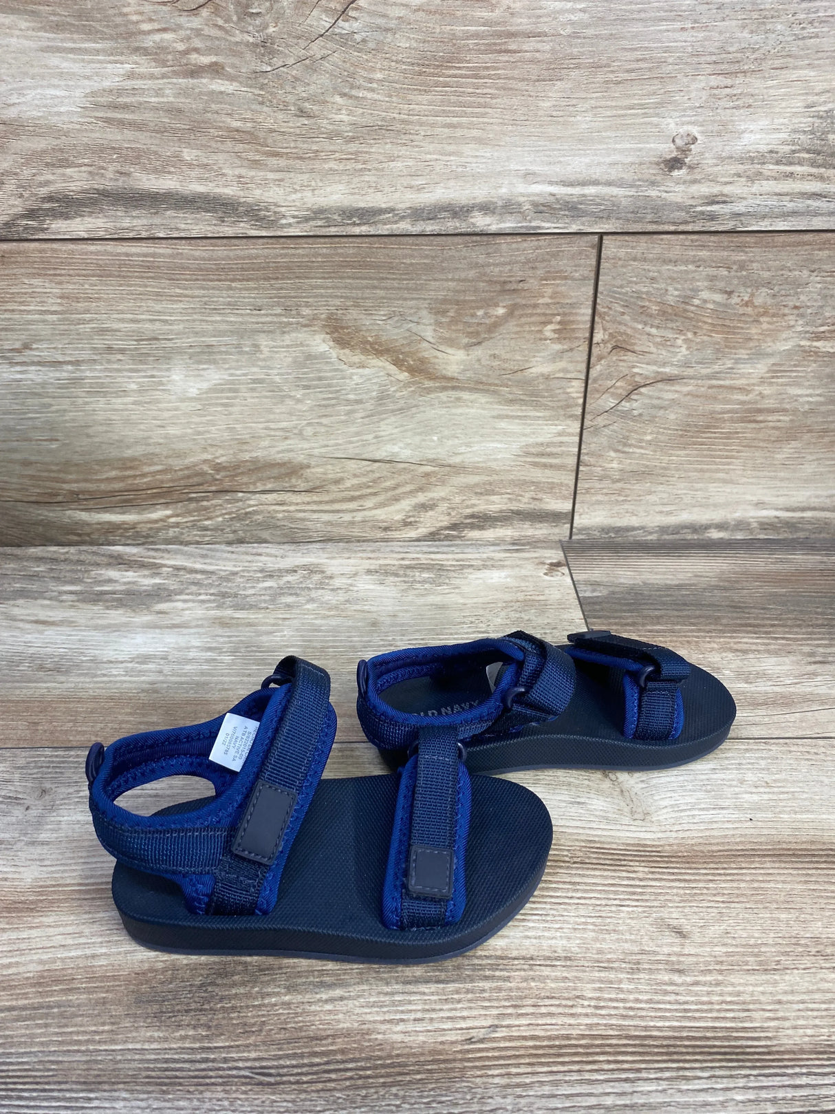 Angled view of Old Navy toddler navy double-strap sandals size 8C showing adjustable Velcro straps and textured footbed on wood floor