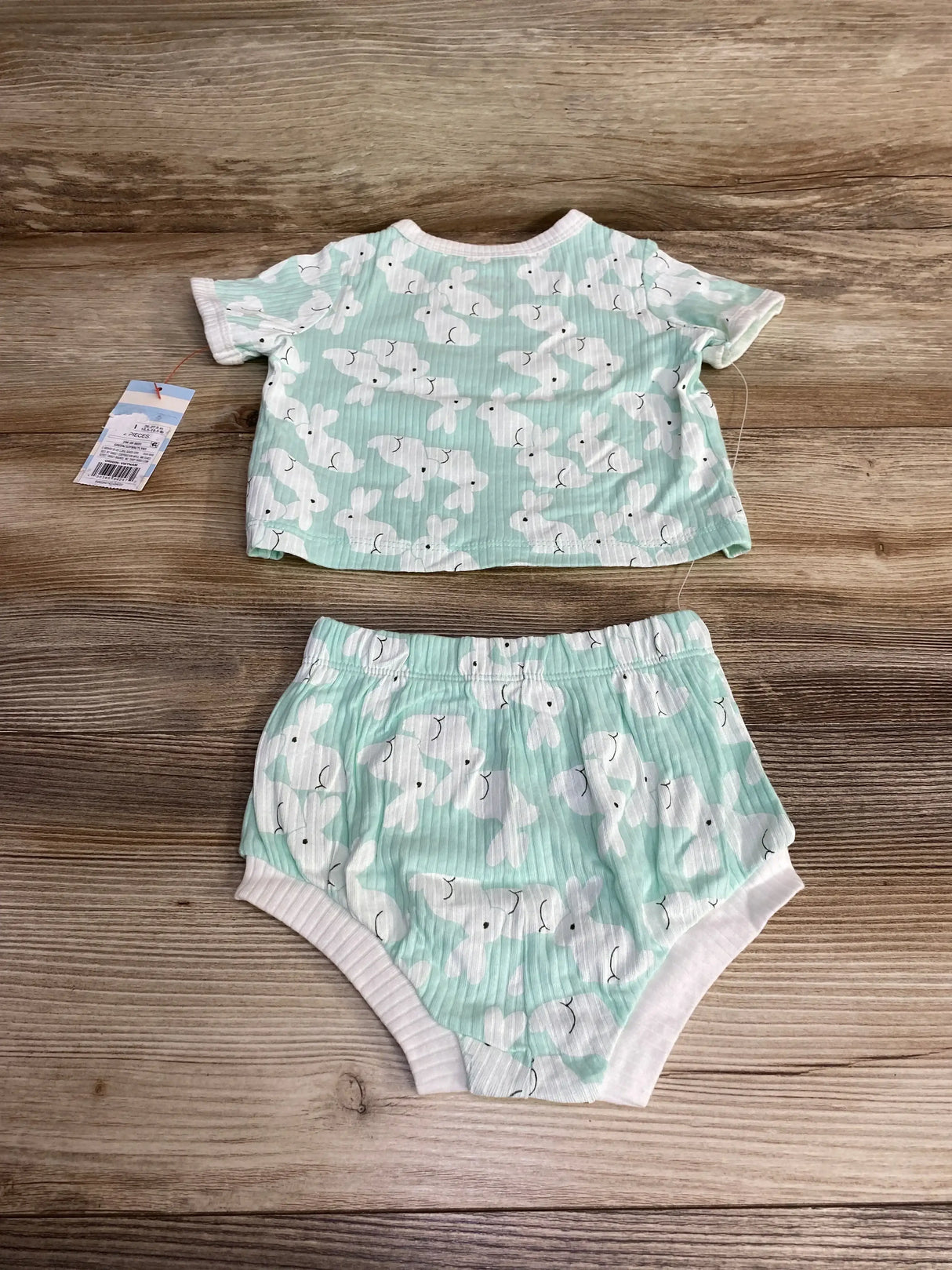 Flat lay of Cat & Jack two-piece mint baby shirt and shorts showing white bunny print and ribbed trim on wood background