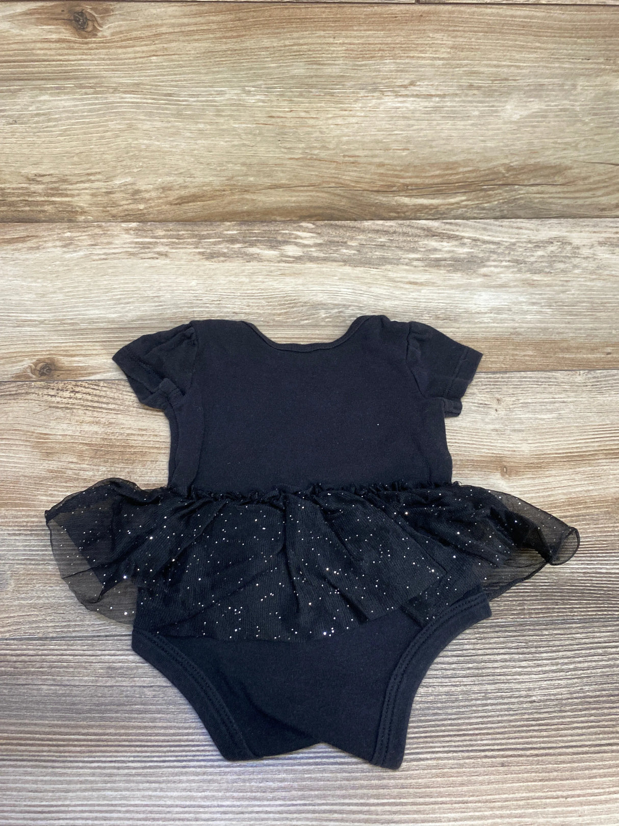Black baby onesie with short sleeves and glittery tulle skirt on wooden floor