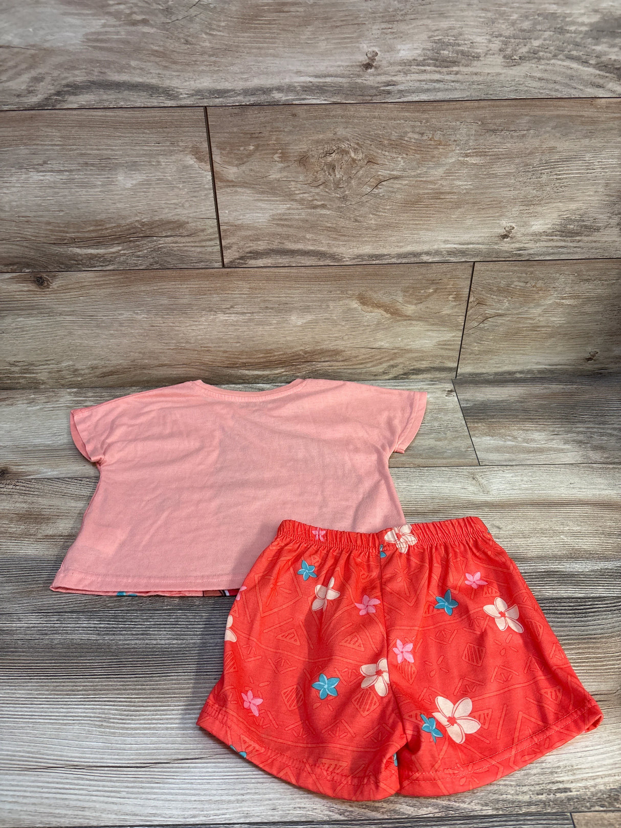 Back view of Moana two-piece peach toddler pajama set with short-sleeve top and floral elastic-waist shorts on wood floor