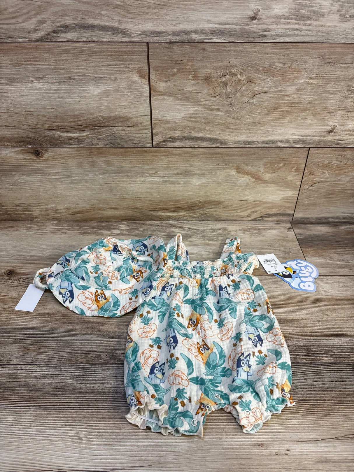 Baby girl Bluey romper with matching bonnet, floral pattern, laid on wood background