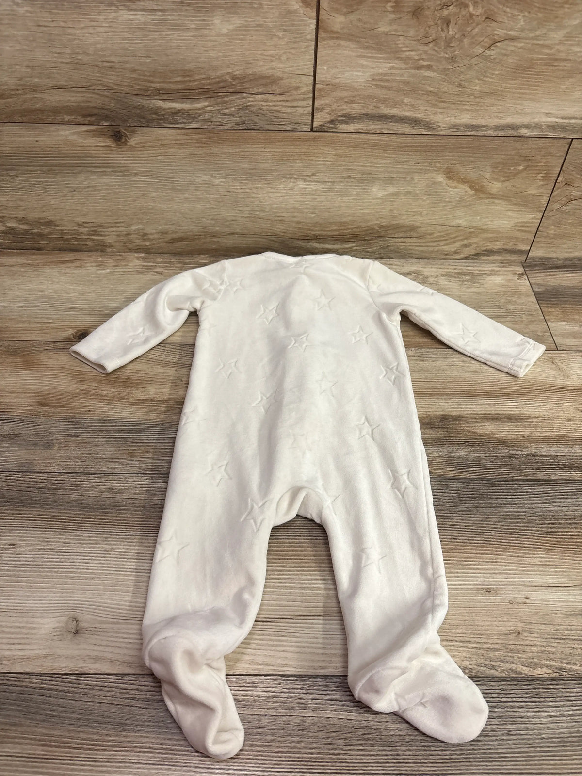 Ivory velour baby sleeper with white star patterns laid flat on a wood floor