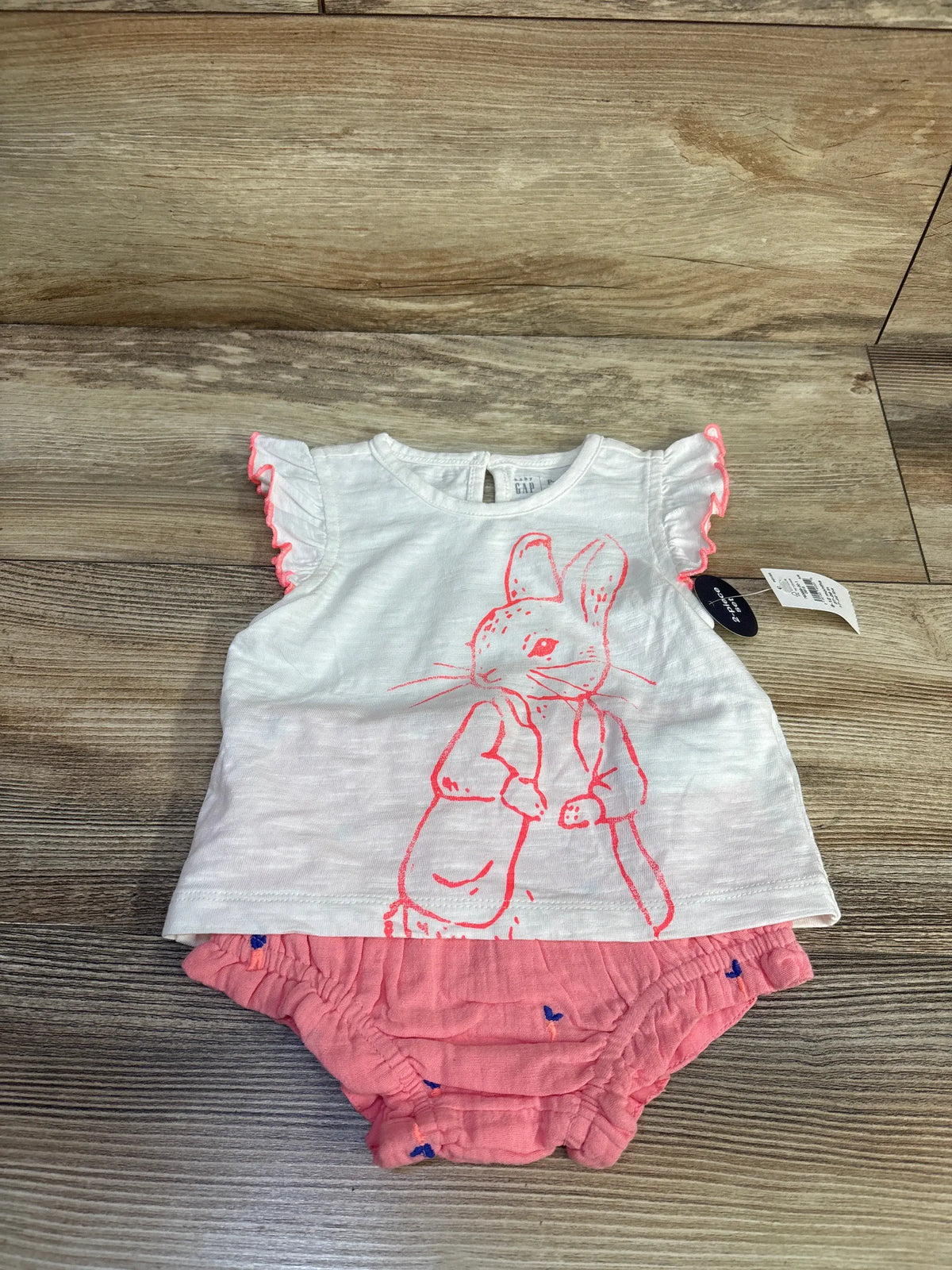 Front view of Baby Gap x Peter Rabbit 2-piece outfit set showing white ruffle-sleeve T-shirt and pink bloomer shorts on wood floor