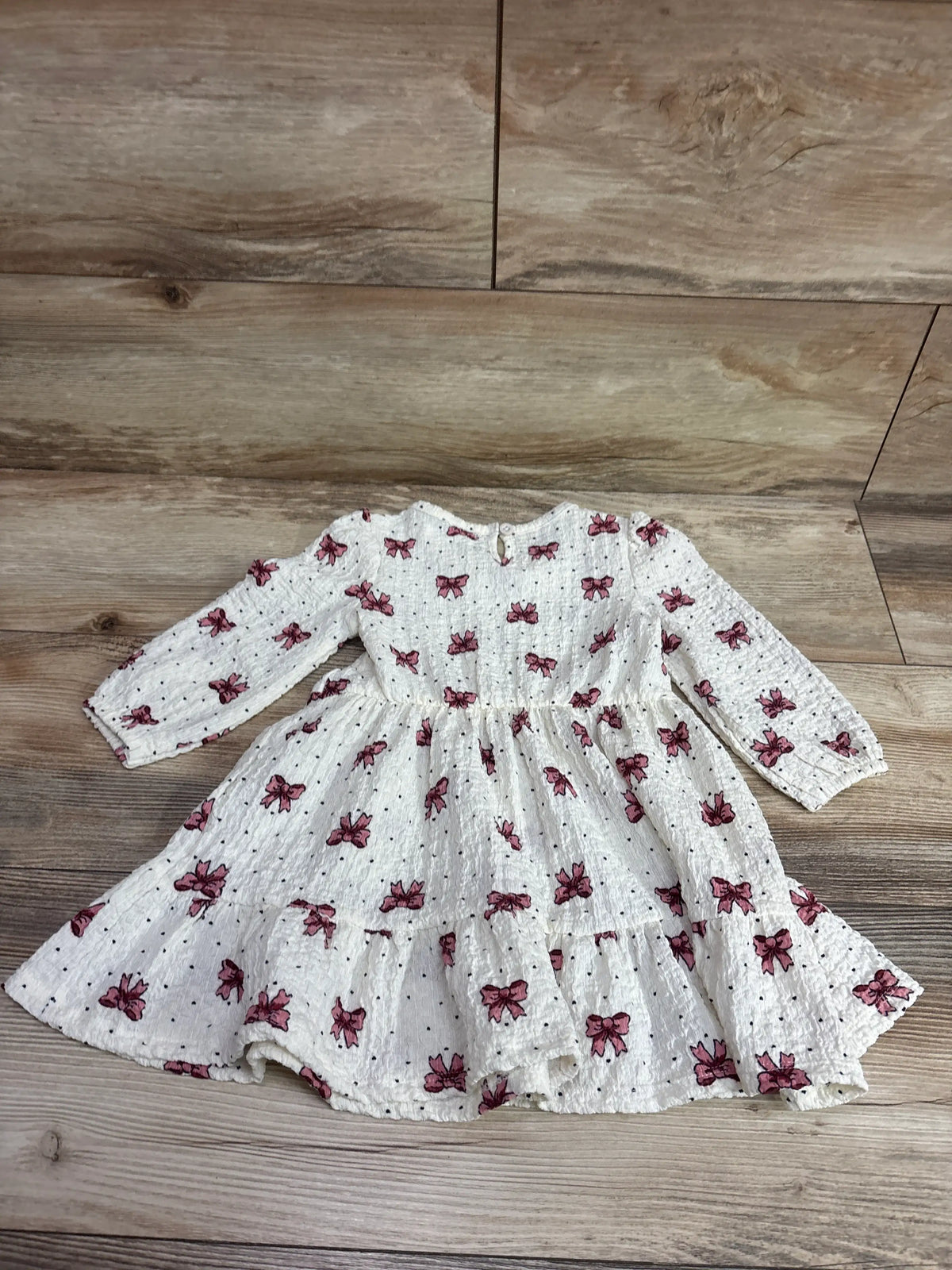 Top view of Nannette bow print long sleeve dress in ivory, showcasing gathered waist and tiered skirt on a wood floor