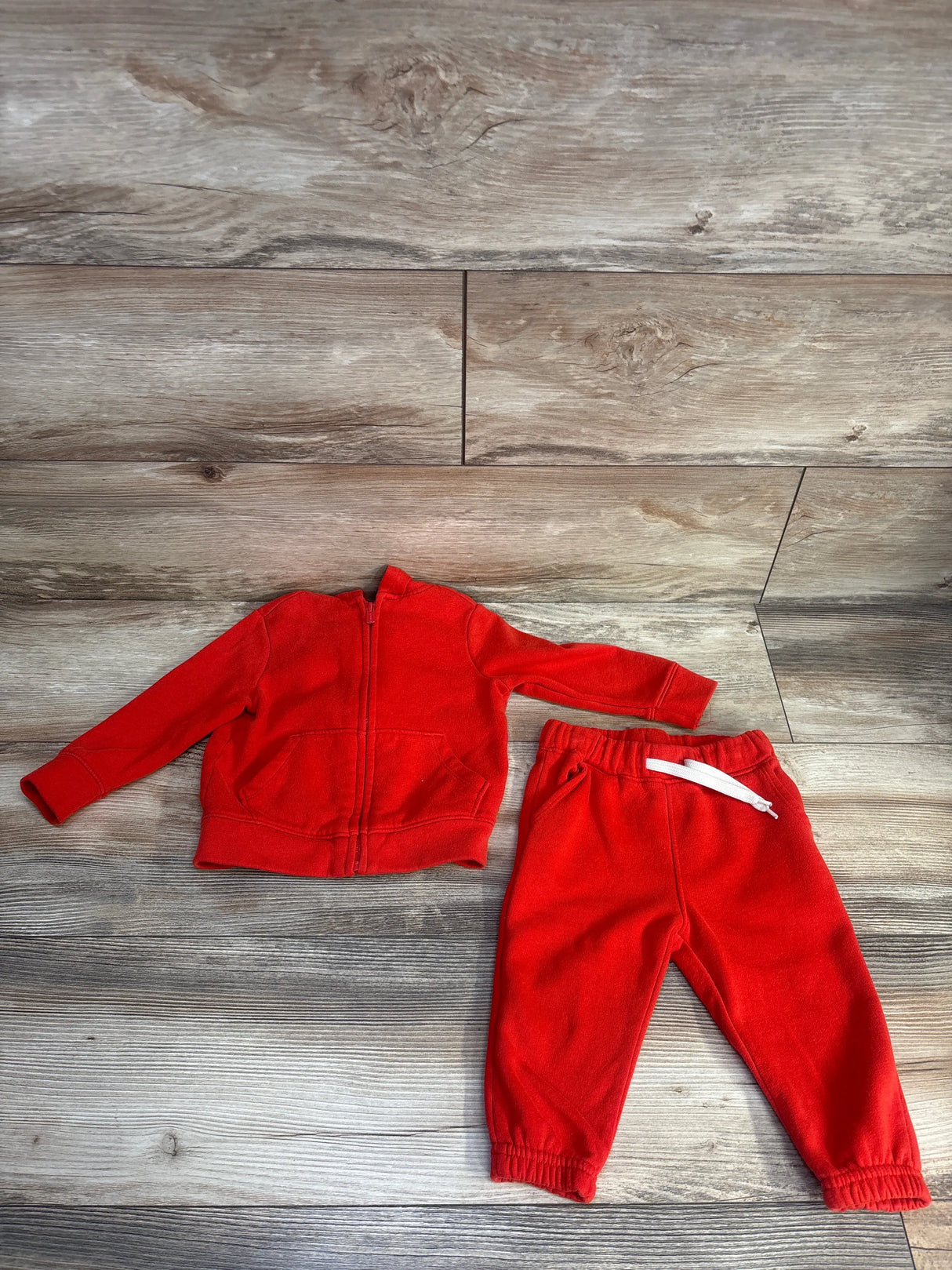 Red toddler tracksuit set with zip-up jacket and pants on wooden floor