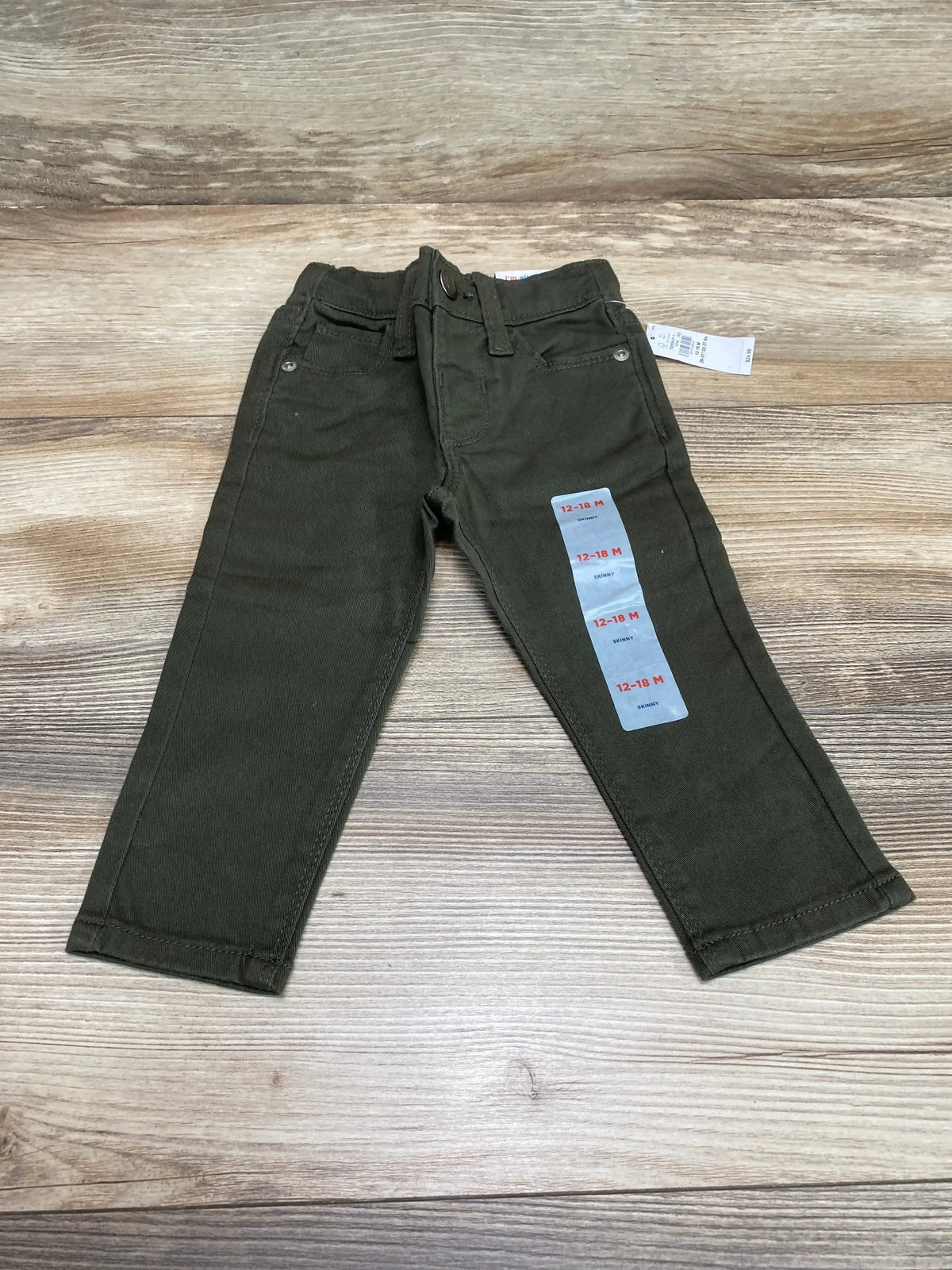 Flat lay of Old Navy olive skinny 360 stretch toddler jeans, size 12-18M, showing front pockets, belt loops and sticker on wooden background