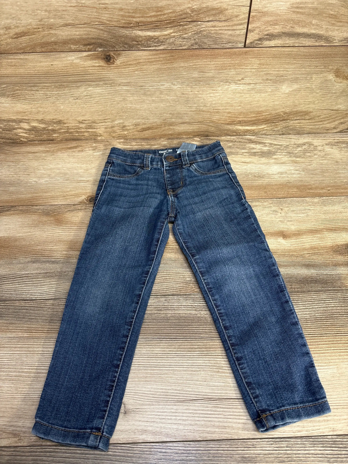 Blue denim kids jeans with front pockets and a button on wooden floor background