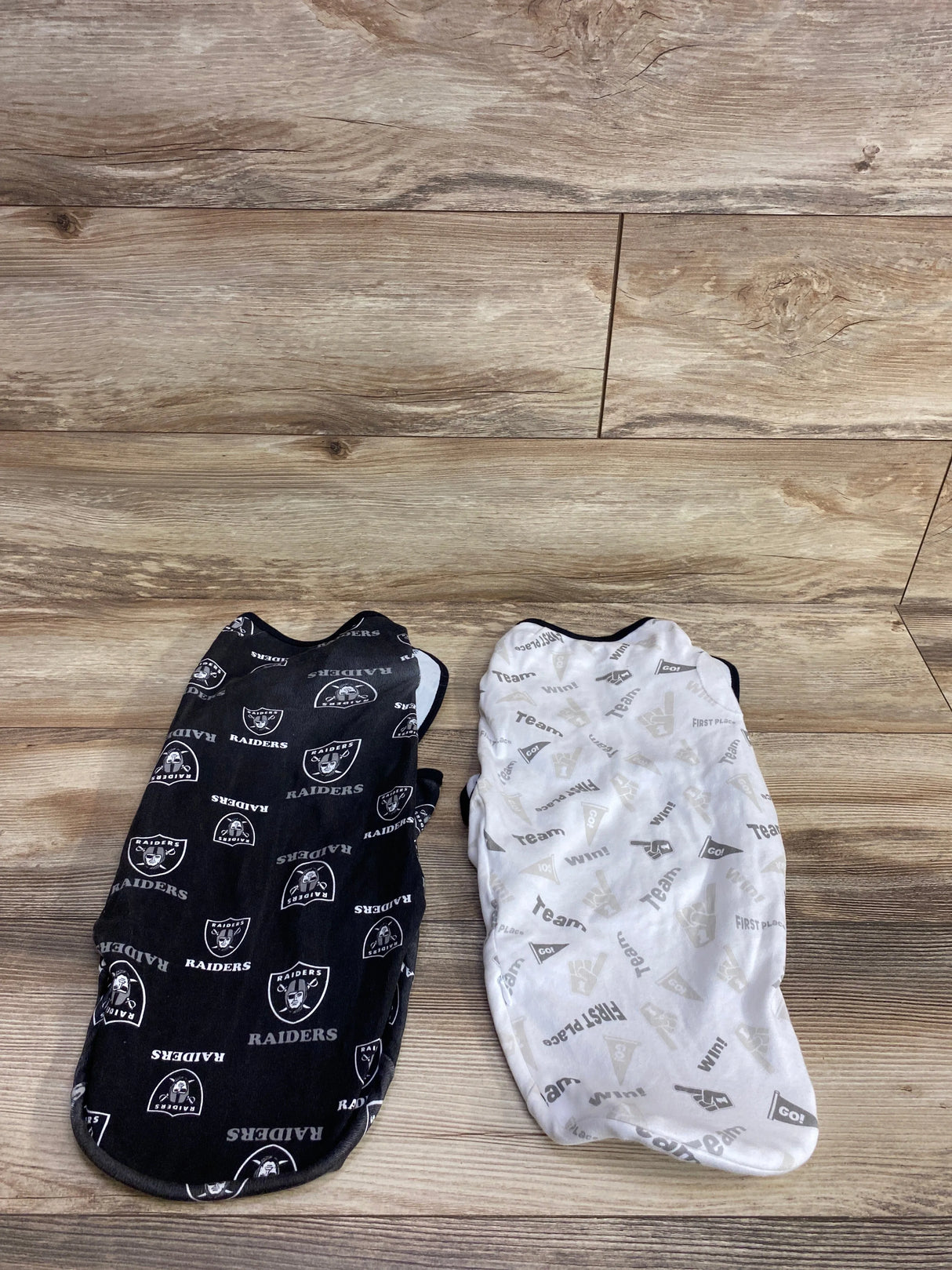 Two infant swaddle blankets with black and white sports-themed prints on wooden floor