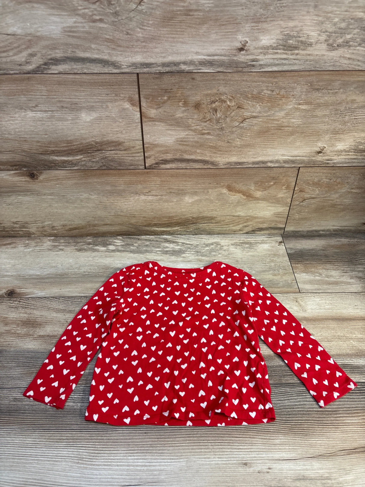 Red long sleeve toddler shirt with white heart pattern on wooden background
