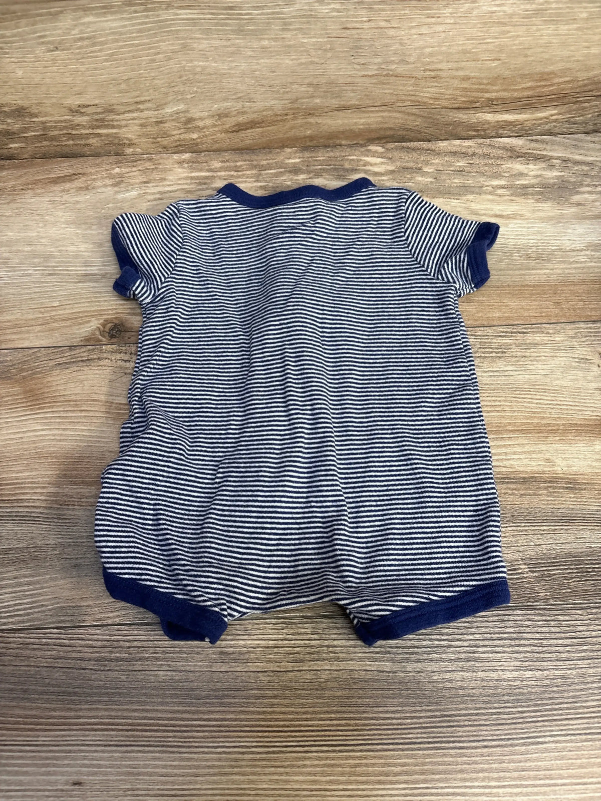 Back view of Carter’s navy and white striped shortie romper showing short sleeves, navy trim, and snap crotch on wood