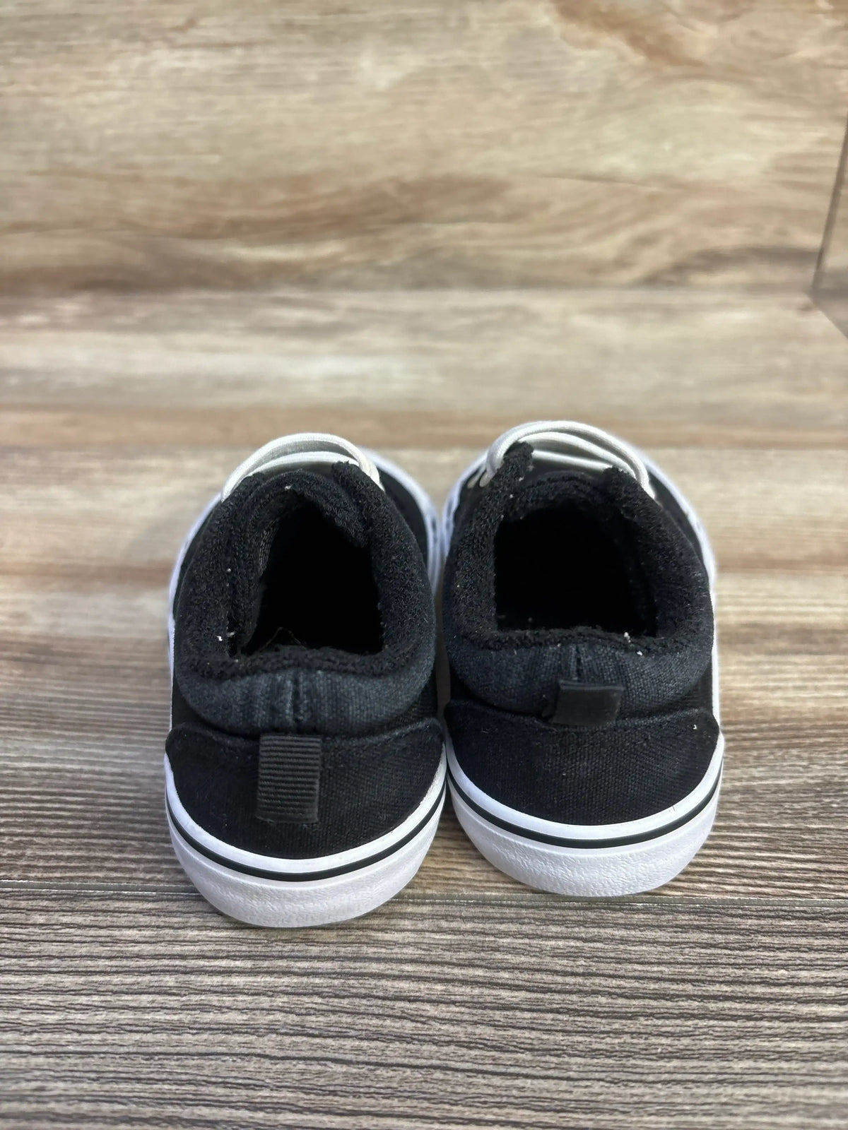 Rear view of Wonder Nation black toddler canvas sneakers showing pull tab and white rubber sole on wood surface