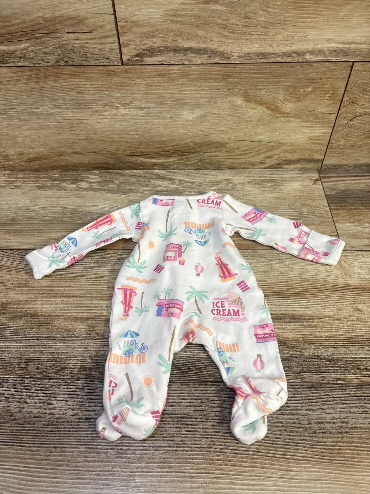 Front view of Child Of Mine white preemie footed sleeper showcasing colorful ice cream print on wood floor