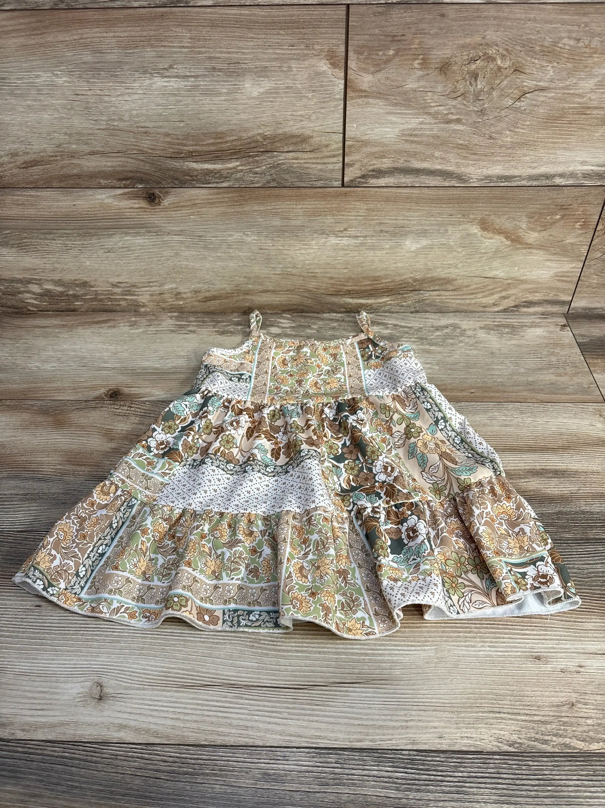 Top down view of beige Tullabee floral tiered 2T dress showing ruffled tiers, thin straps and patchwork print on wood floor