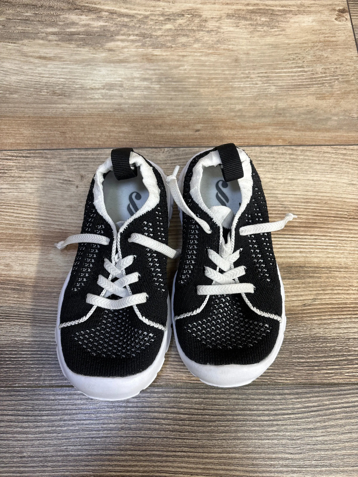 Front view of Eqw slip-on sneakers showcasing black uppers, white soles, and pull tabs on a wood-grain background