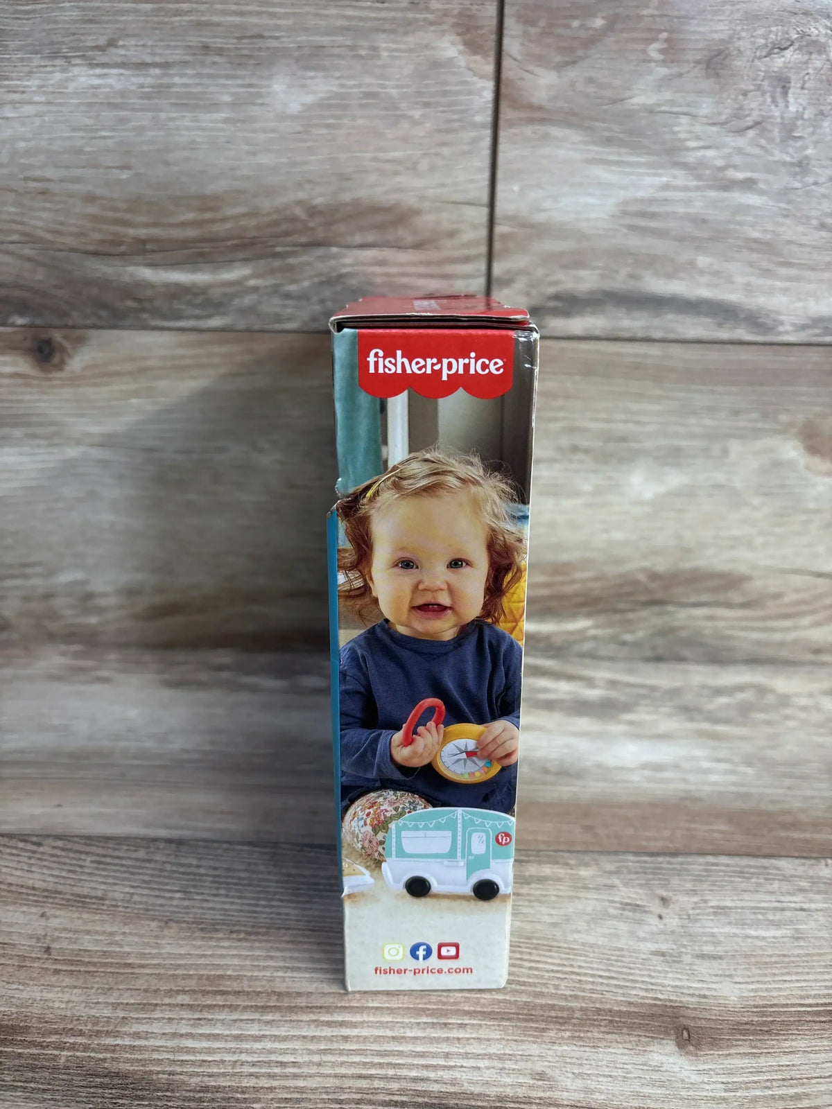 Side view of NEW Fisher Price S'more Fun Camping Gift Set 3pc showcasing box panel with Fisher-Price logo smiling baby holding compass toy with wood plank background