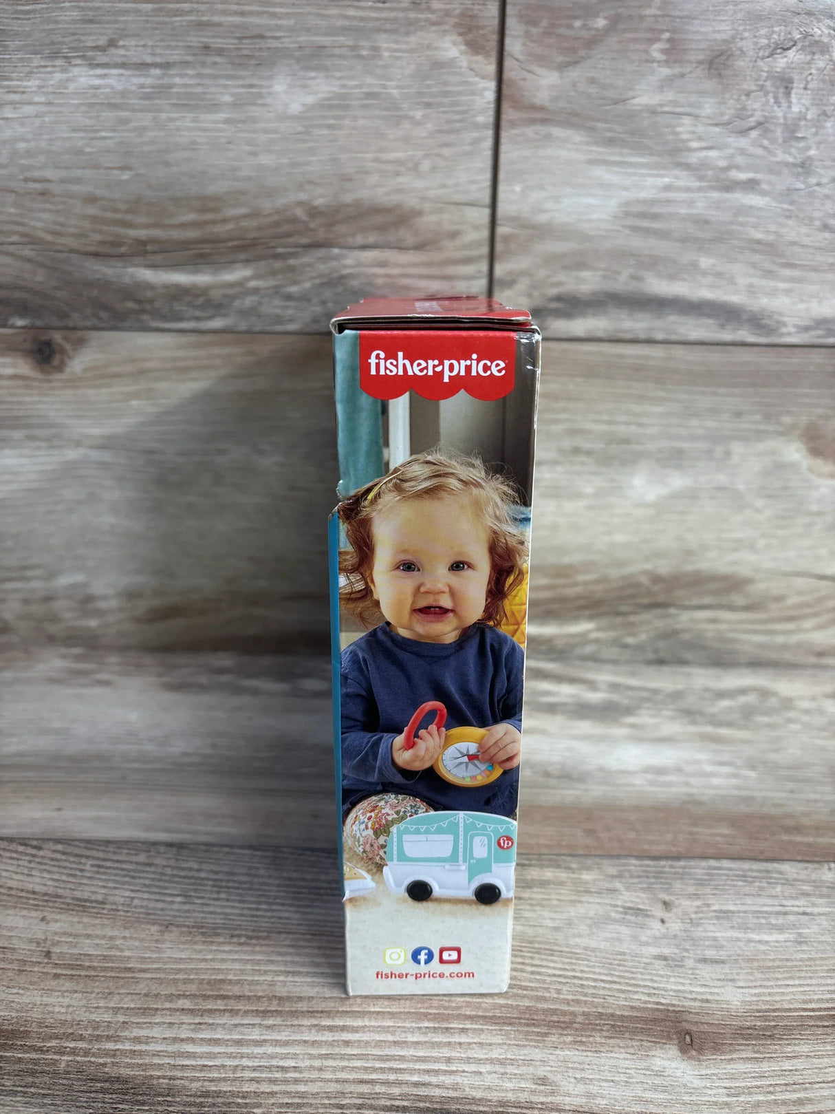 Side view of NEW Fisher Price S'more Fun Camping Gift Set 3pc showcasing box panel with Fisher-Price logo smiling baby holding compass toy with wood plank background