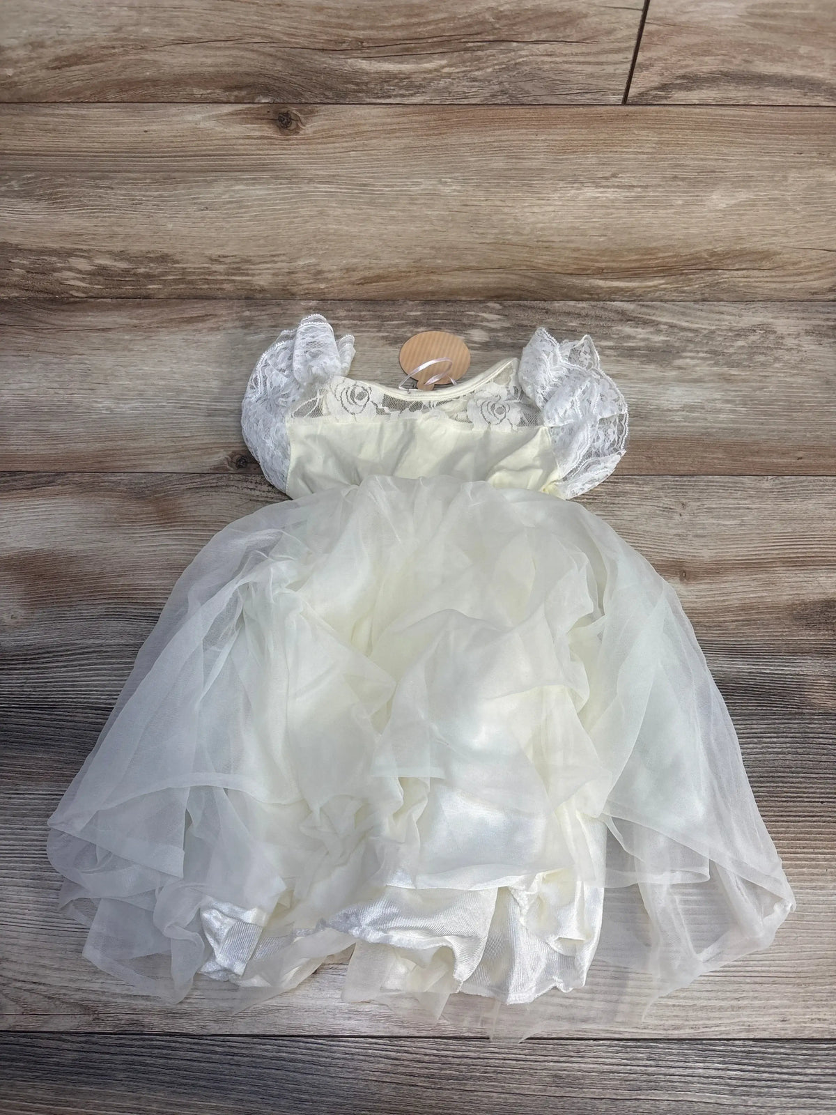 White baby dress with lace sleeves and layered tulle skirt on wooden background