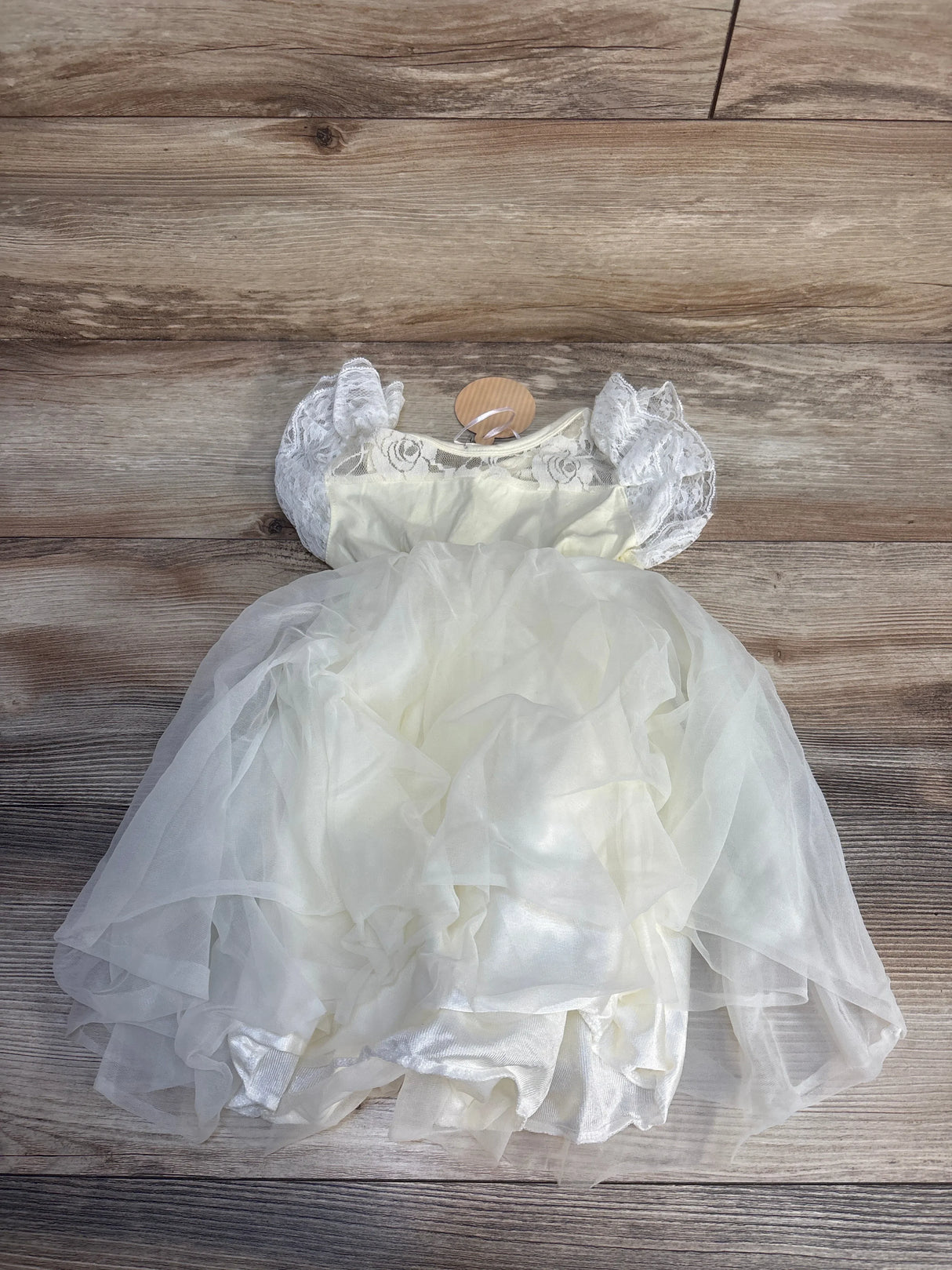 White baby dress with lace sleeves and layered tulle skirt on wooden background