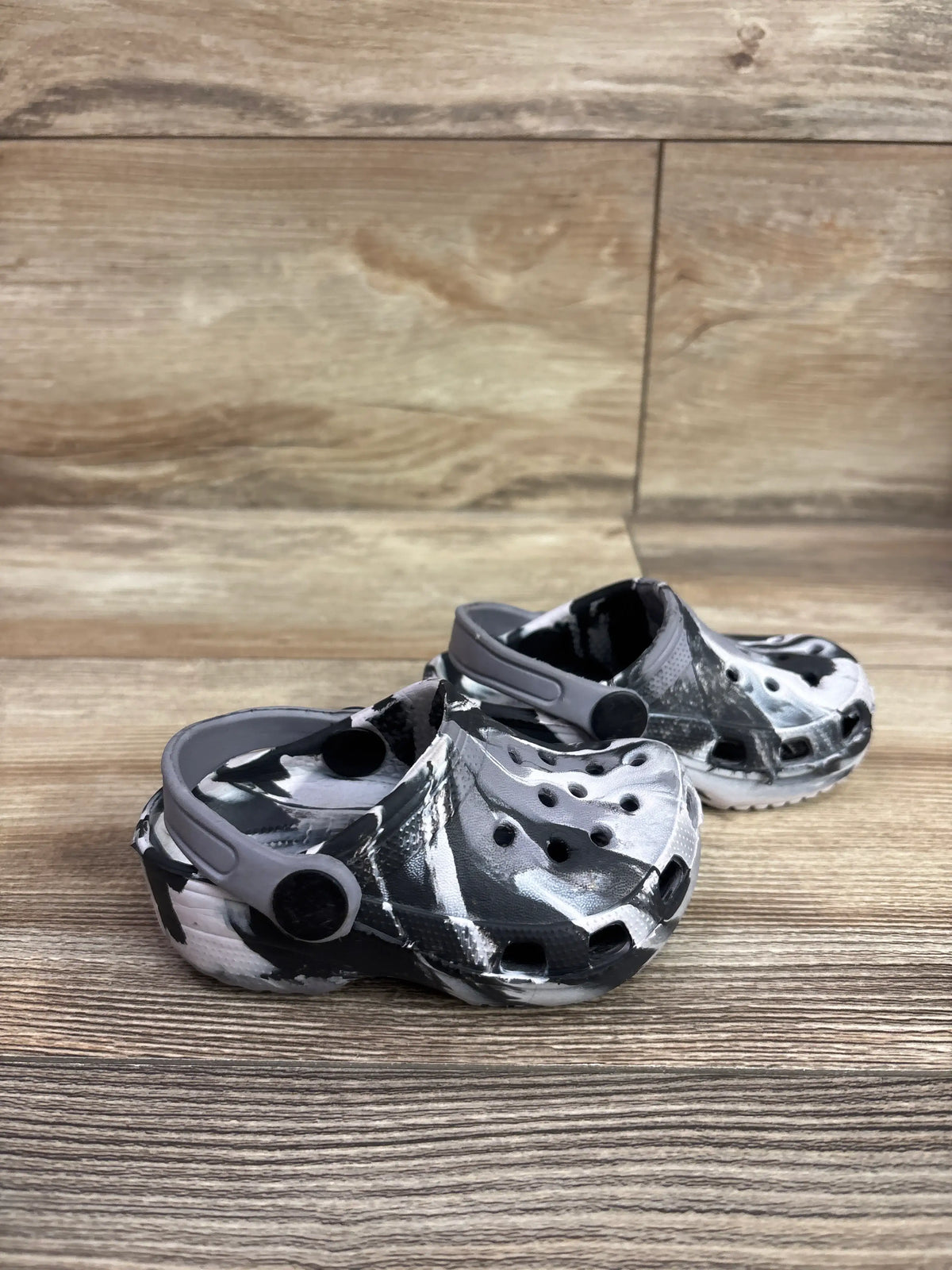 Three-quarter view of black and white marbled clogs, size 5C, showcasing perforated uppers and heel straps on a wood surface