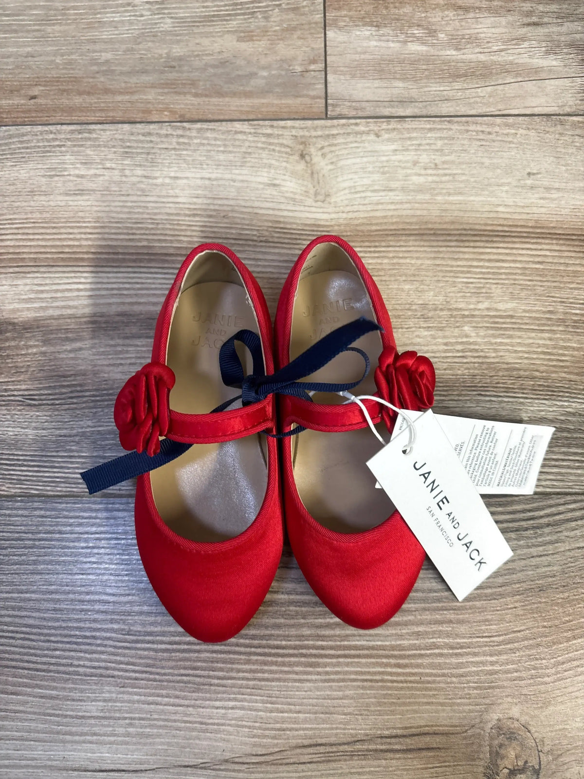Top view of Janie and Jack red satin rosette ballet flats size 7C showcasing rosette strap and navy ribbon bow on wood floor