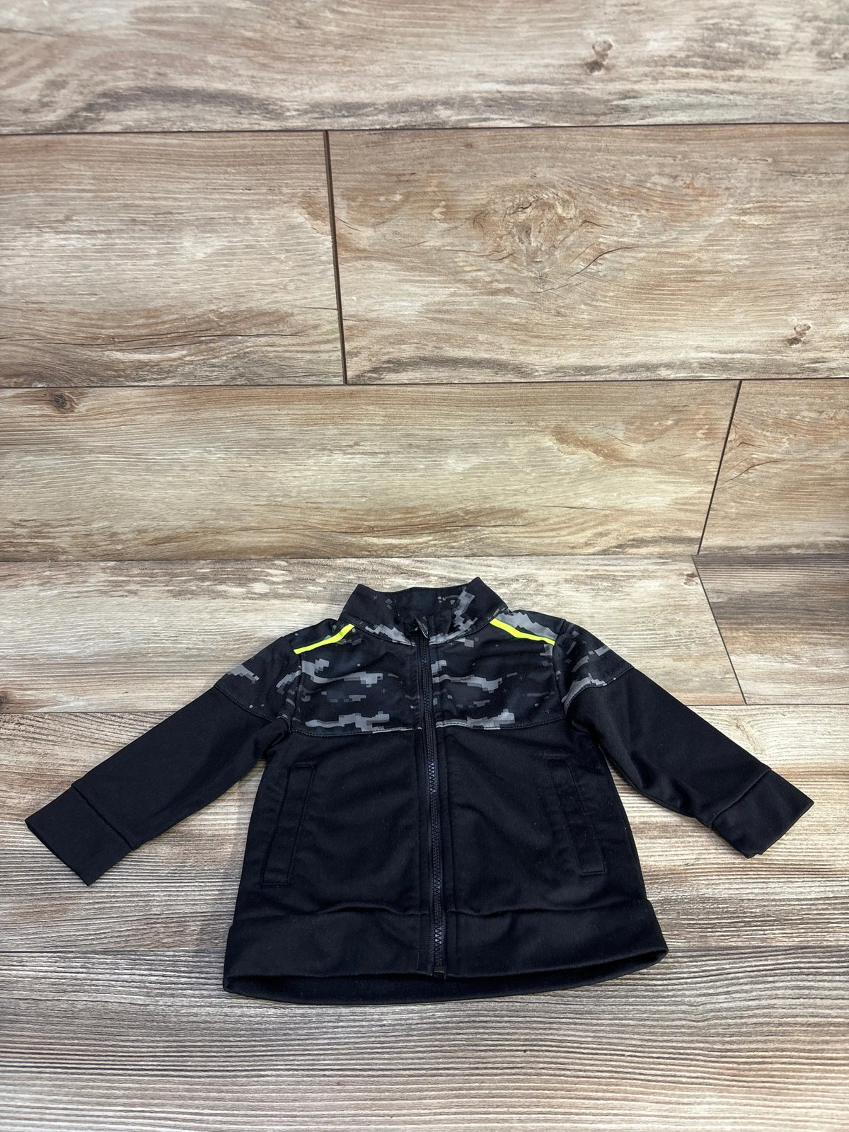 Front view of black Athletic Works full zip active jacket showcasing gray camouflage panels and neon yellow accents on wood flooring