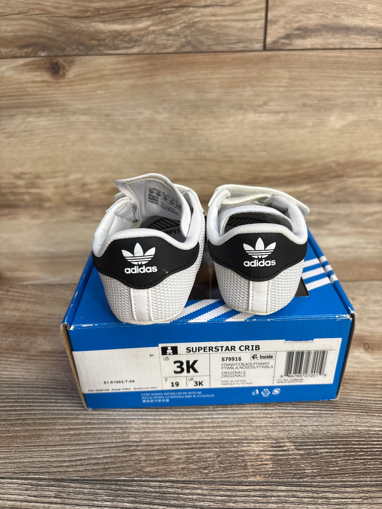 Adidas Superstar Crib baby shoes in white and black on blue shoe box, size 3K, wooden background