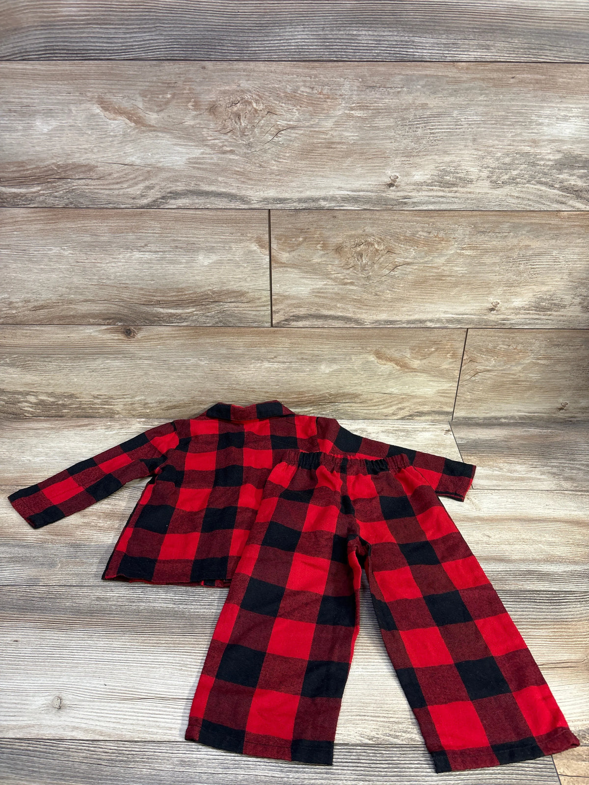 Flat lay of red-and-black buffalo plaid 2-piece pajama set with collared top and elastic-waist pants on wood background
